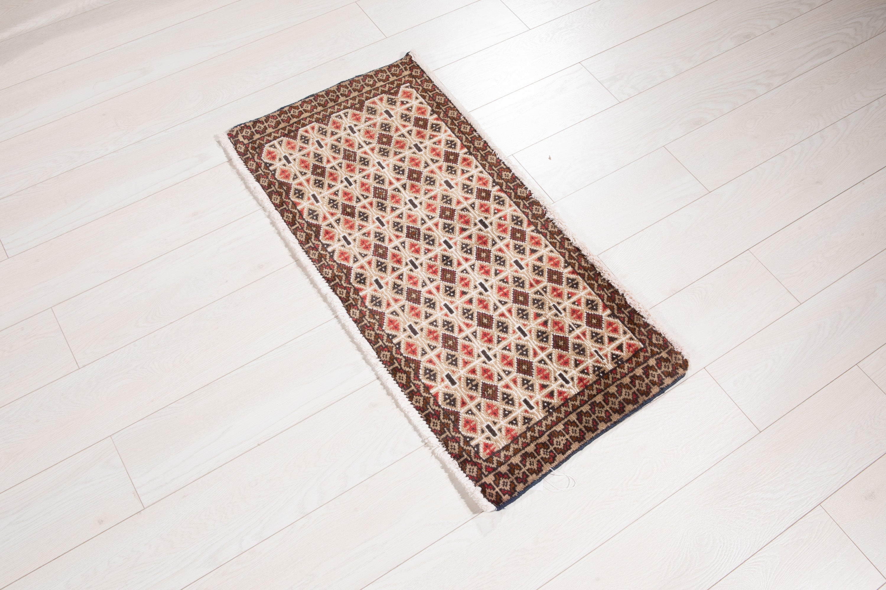Angled view of the full beige and brown Persian rug on a wood floor, showing its diamond pattern.