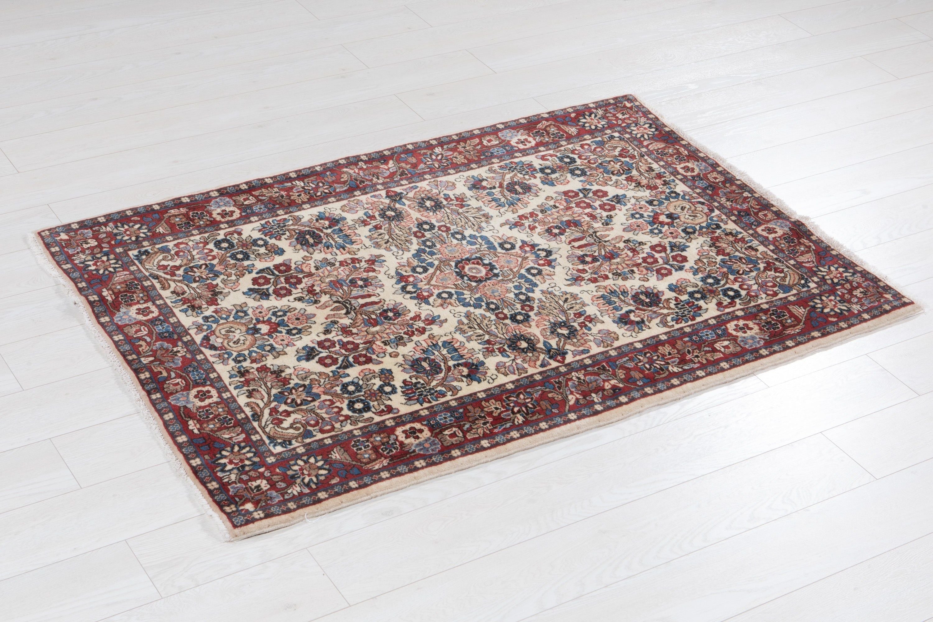 Angled view of the full beige Sarough rug on a wood floor, showing the red floral border.
