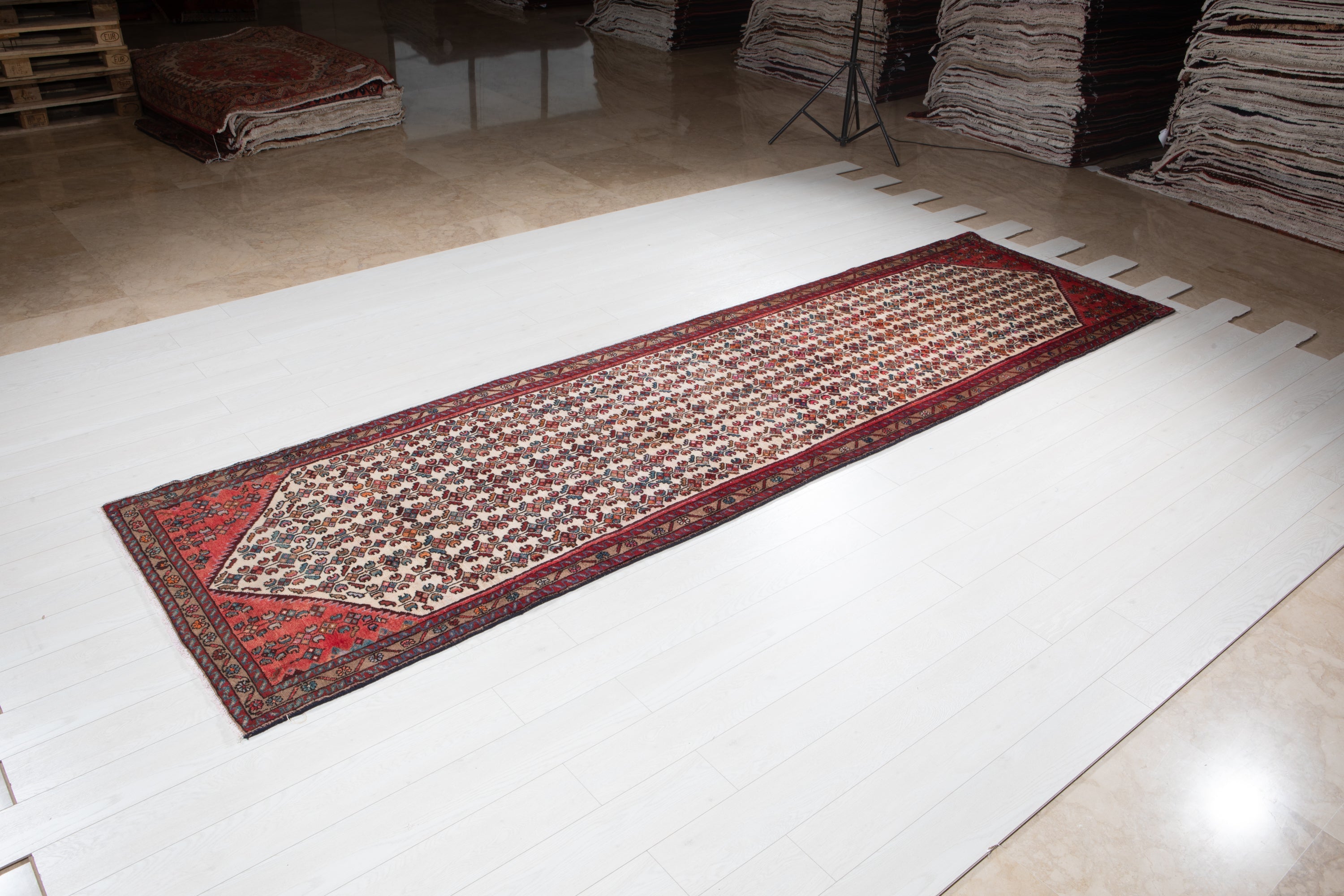 Hamadan Persian runner rug displayed on showroom floor with rolled rugs in background