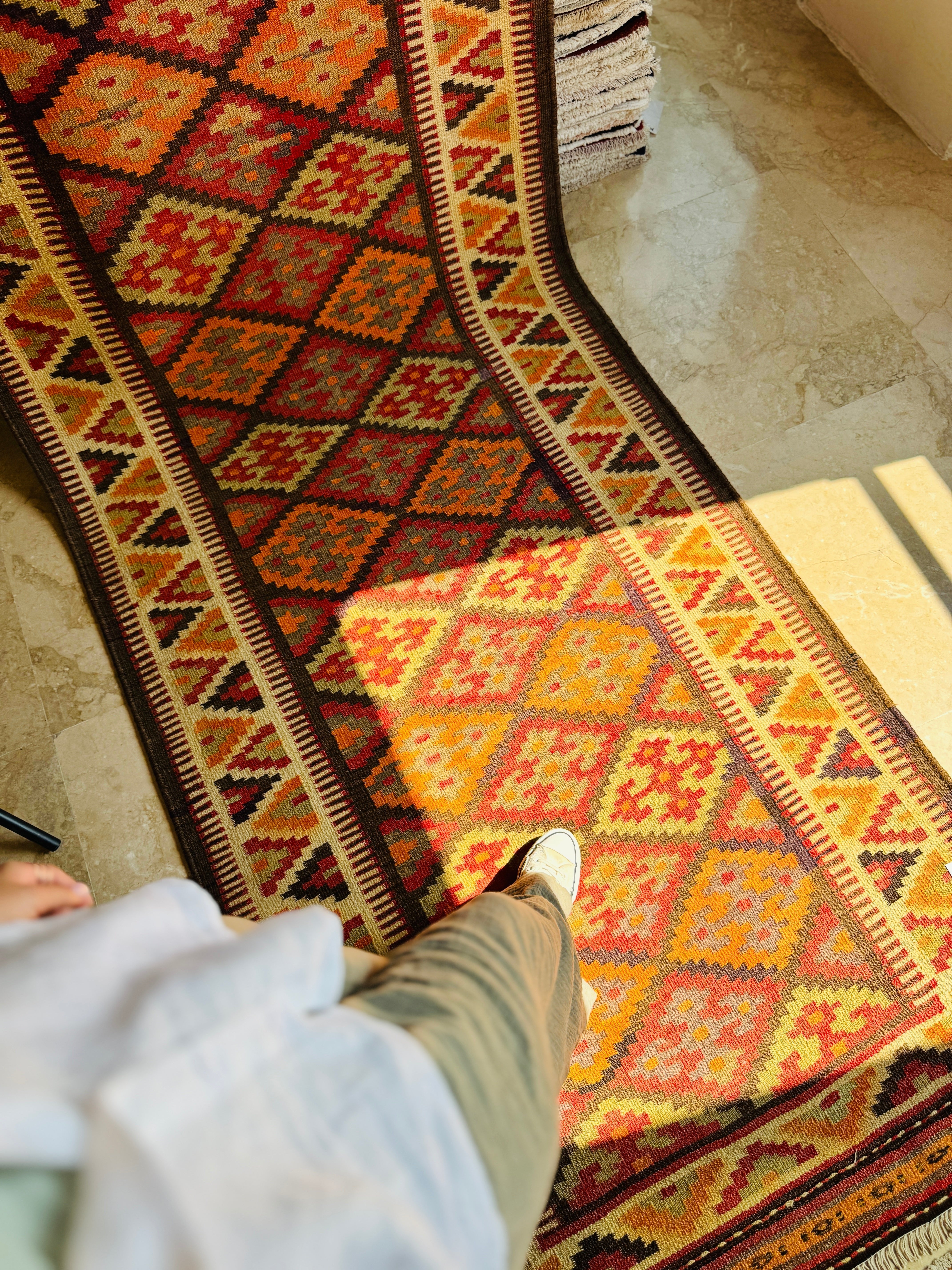 Lifestyle shot of a person walking across the orange kilim runner in sunlight.