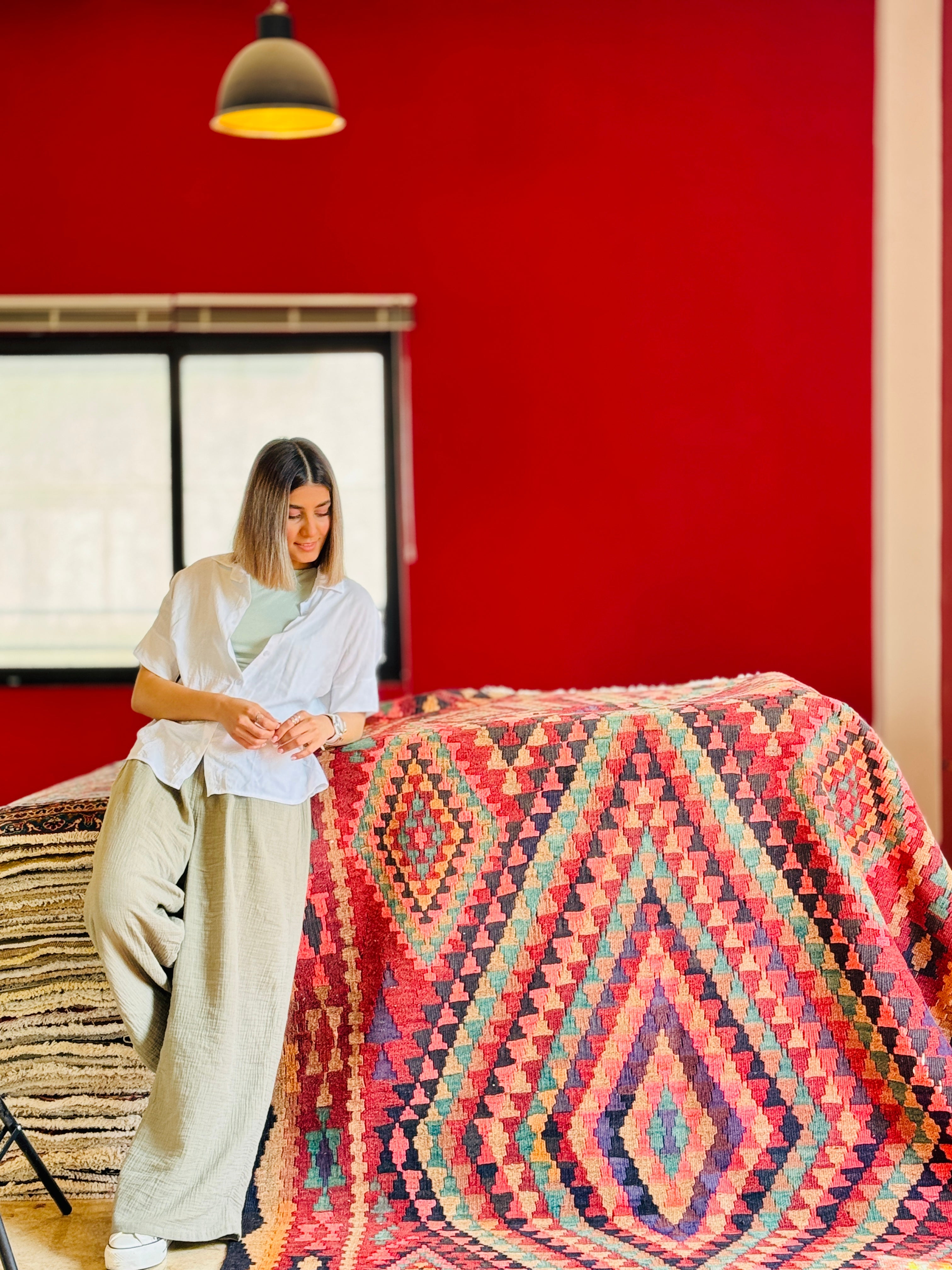 Studio photo shoot of the colorful Shiraz kilim rug draped over furniture beside a woman.