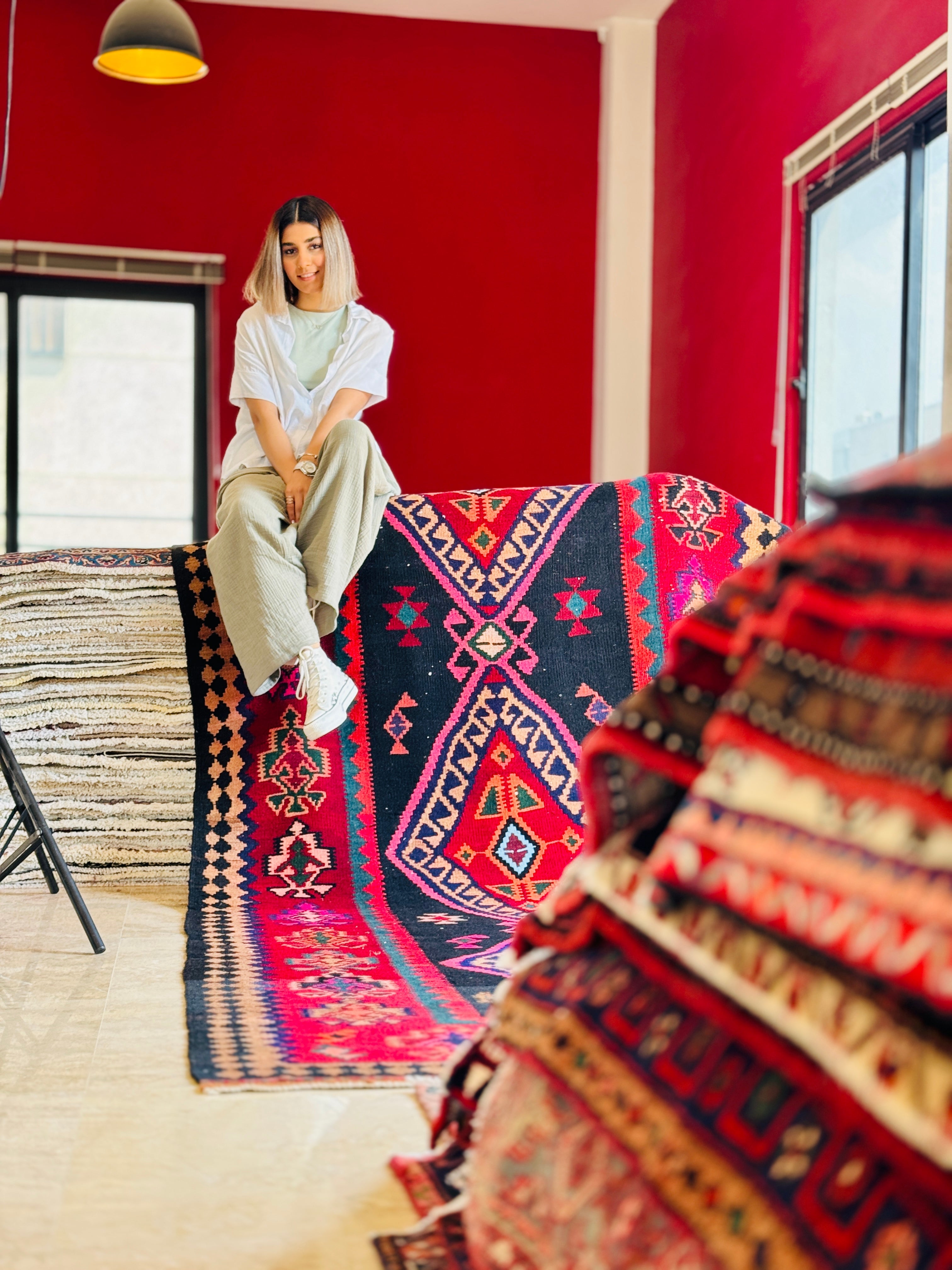 Studio photo shoot of a woman sitting on the red and navy kilim rug.