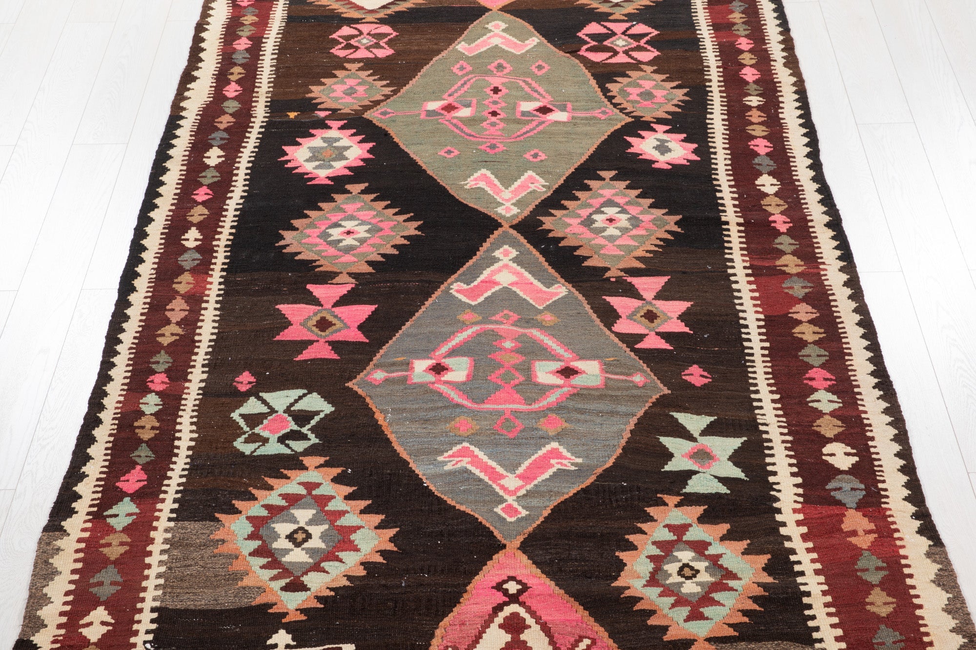 Top-down view of the Persian kilim rug's diamond medallions and geometric border pattern.
