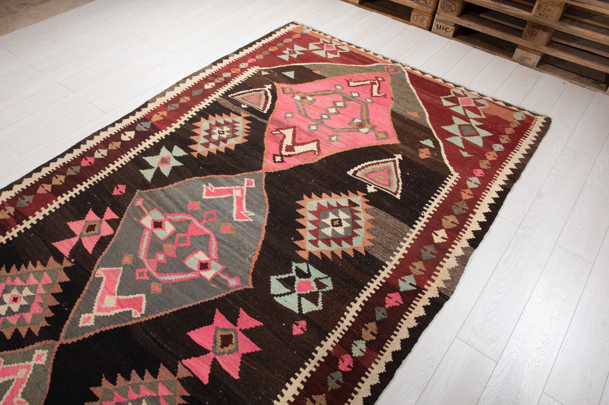 Warehouse angle shot of the vintage kilim rug's diamond medallions on the showroom floor.