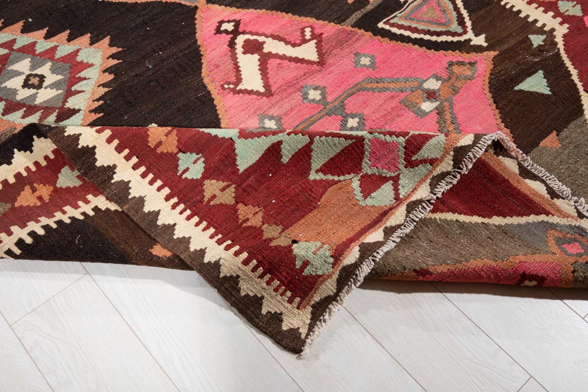 Corner folded back to show the kilim's flatwoven reverse side and fringe edge.