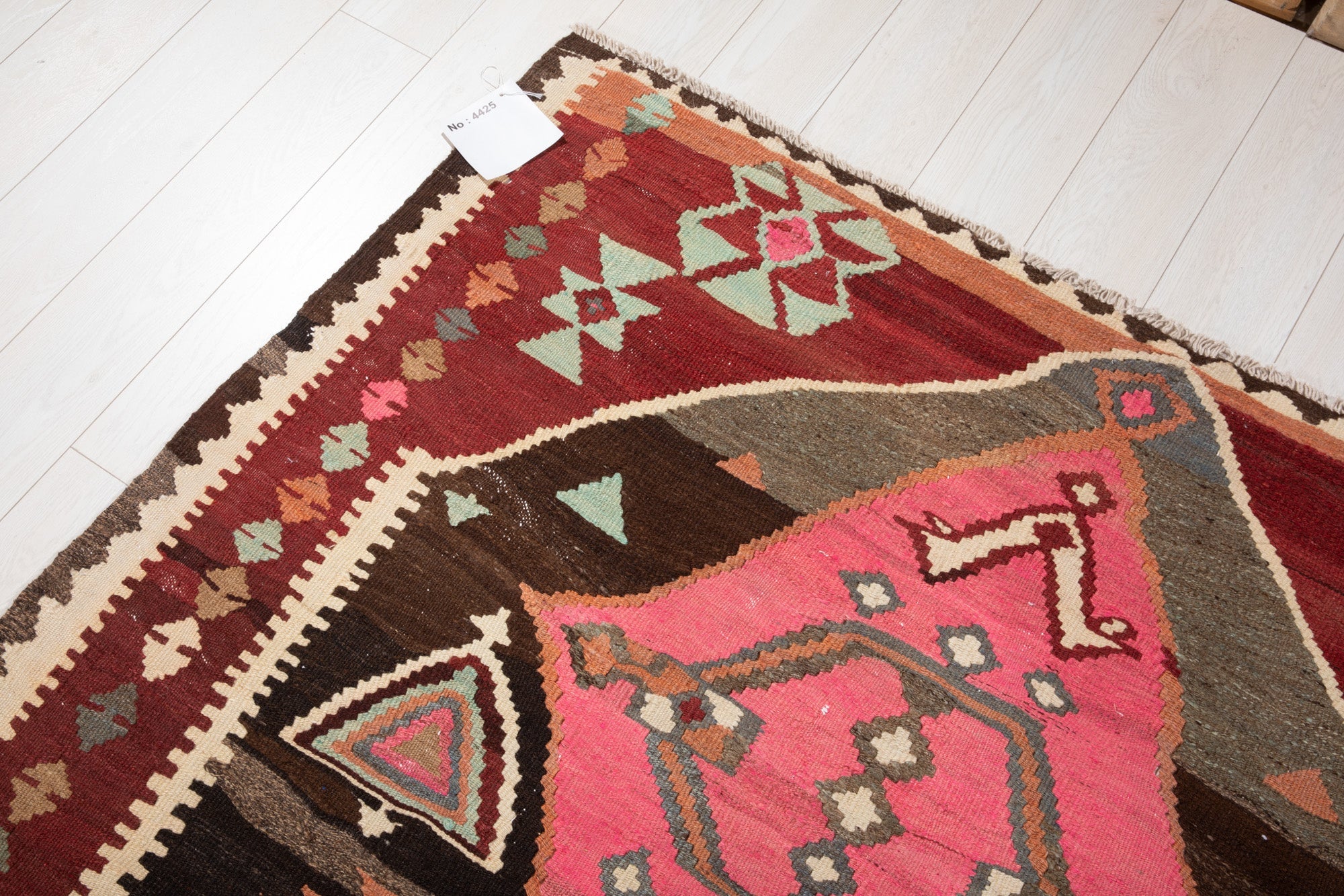 Corner of the vintage Persian kilim runner with an attached inventory identification tag.