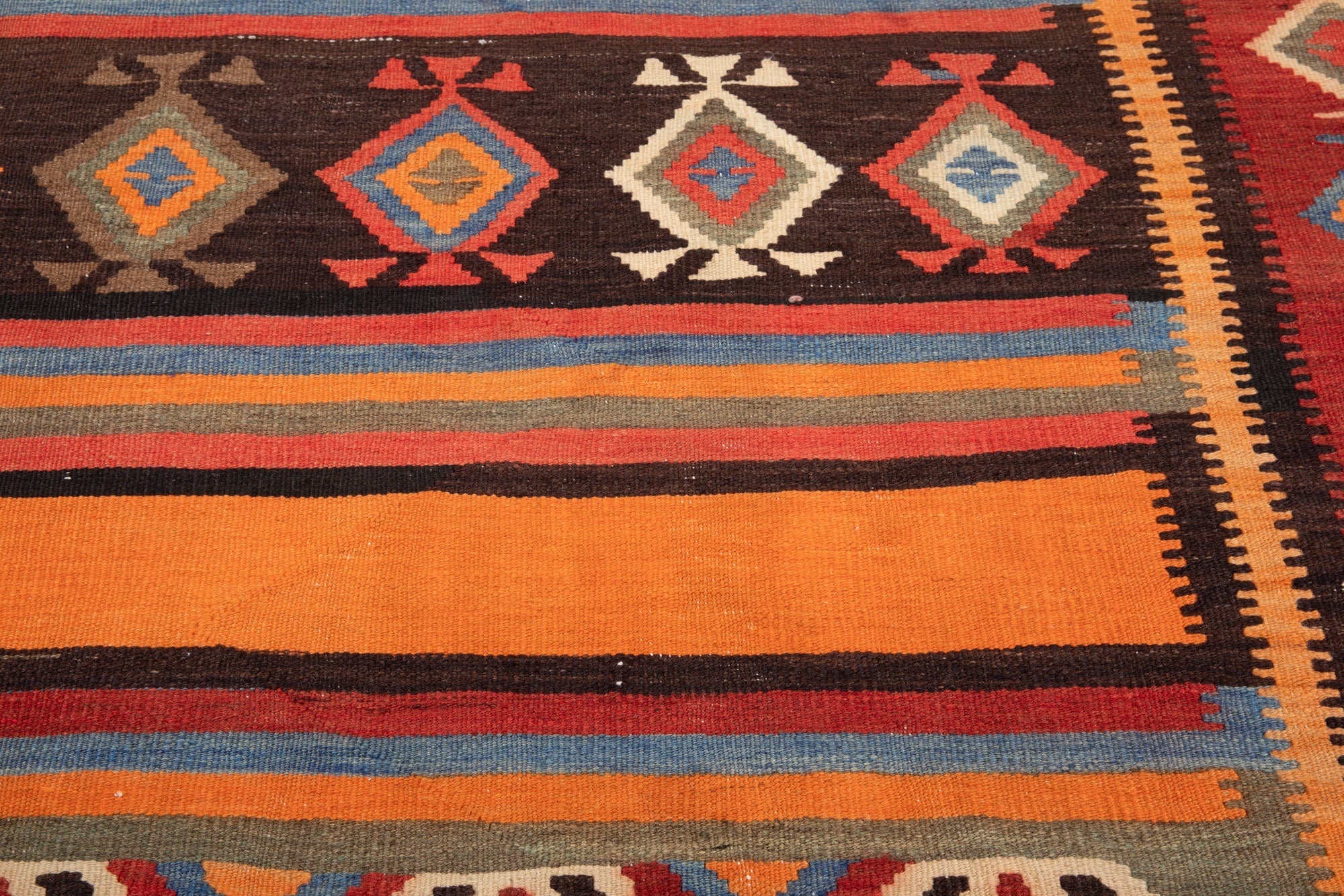 Close-up texture of the kilim's diamond motifs and multicolor striped weave.