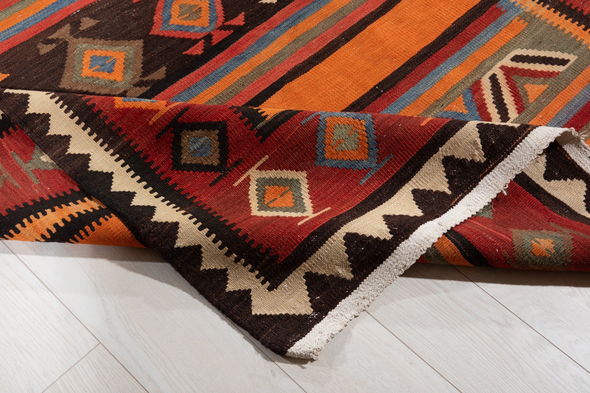 Corner of the kilim rug folded up, showing its striped design and fringed edge.