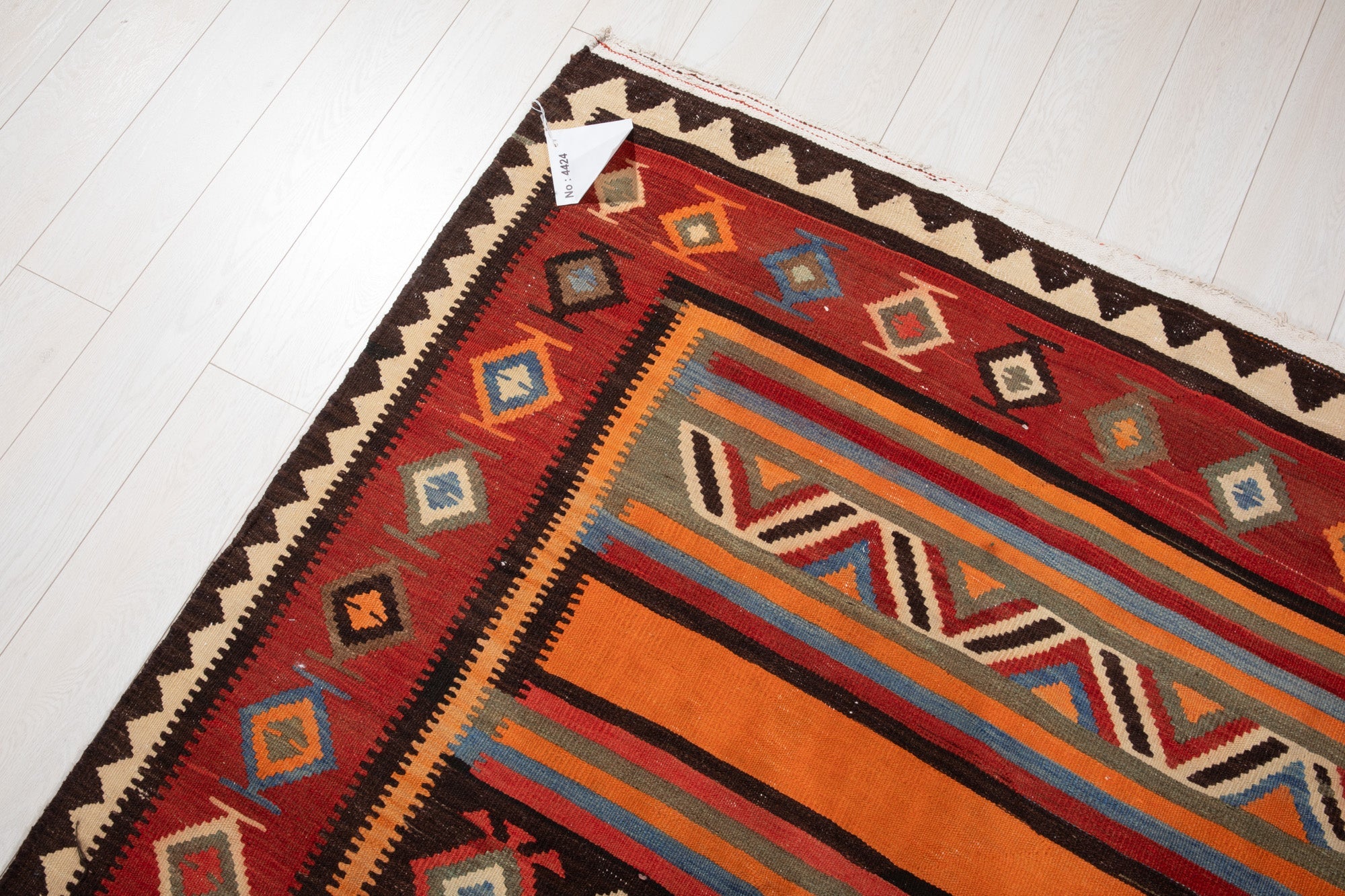 Corner of the vintage Persian kilim rug with an attached inventory identification tag.
