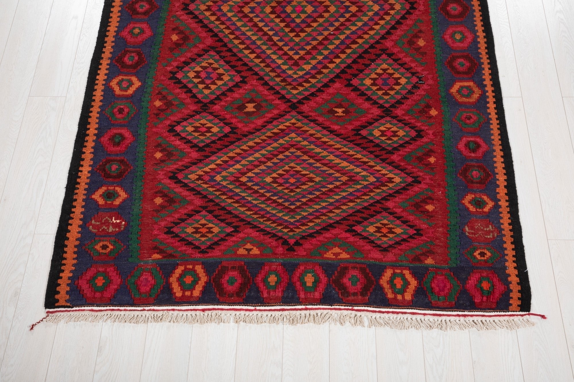 Floor-level view of the kilim's fringed end and hexagon border pattern.