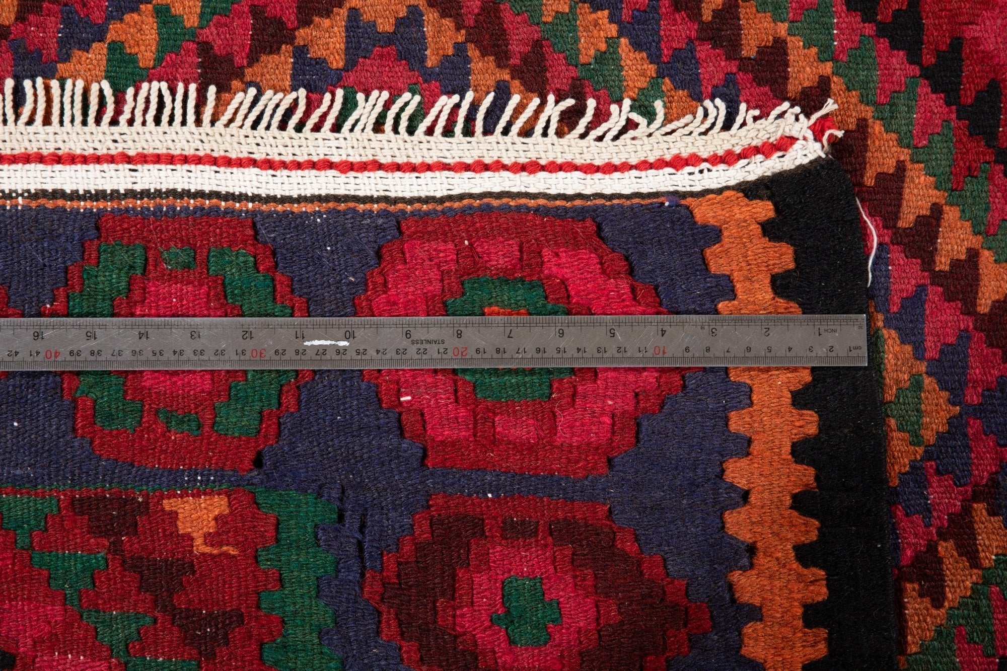 Ruler measuring the kilim's border width next to its fringe.