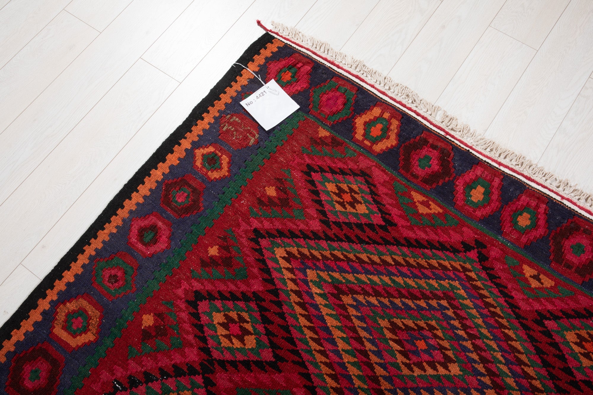 Corner of the vintage Persian kilim rug with an attached inventory identification tag.