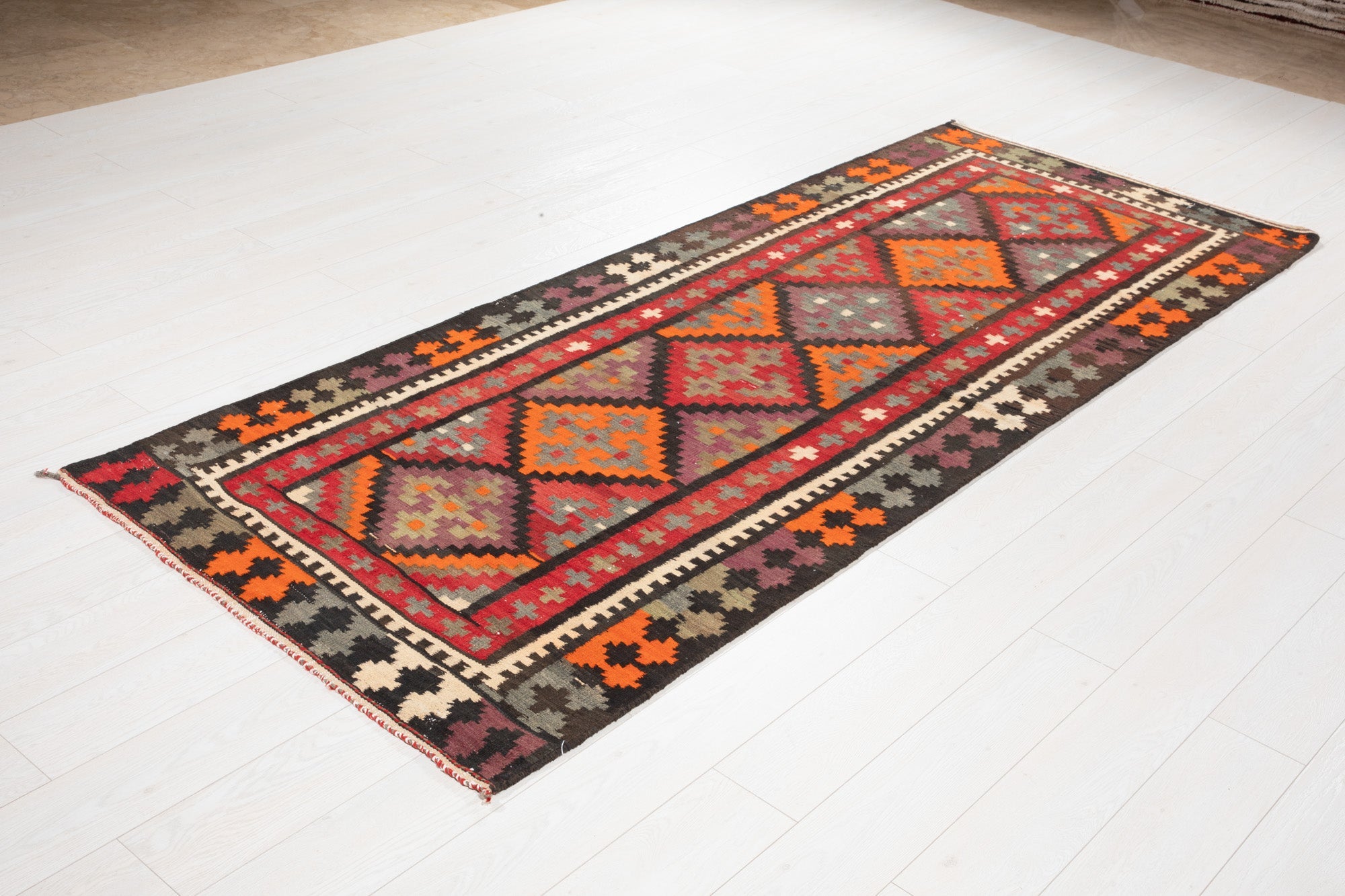 Angled view of the Persian kilim runner's diamond medallions on a wood floor.