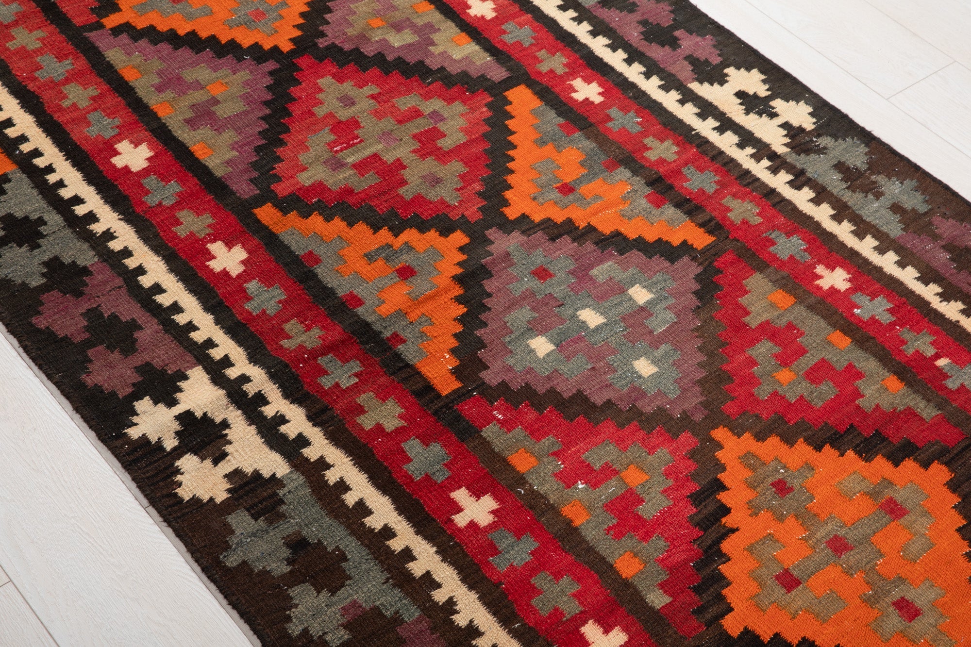 Diagonal close view of the kilim's orange diamond medallions and cross motifs.