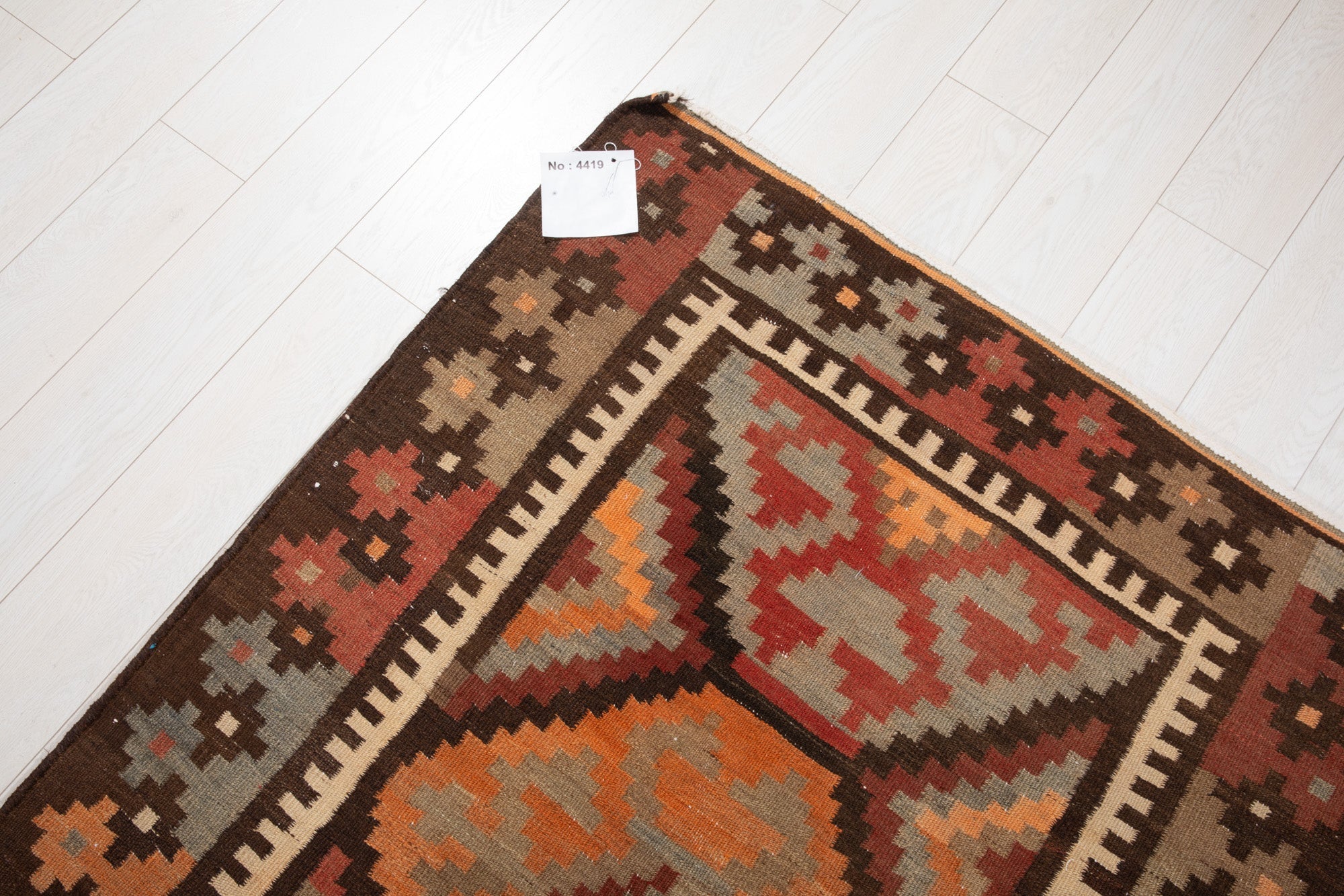 Corner of the antique Persian kilim rug with an attached inventory identification tag.