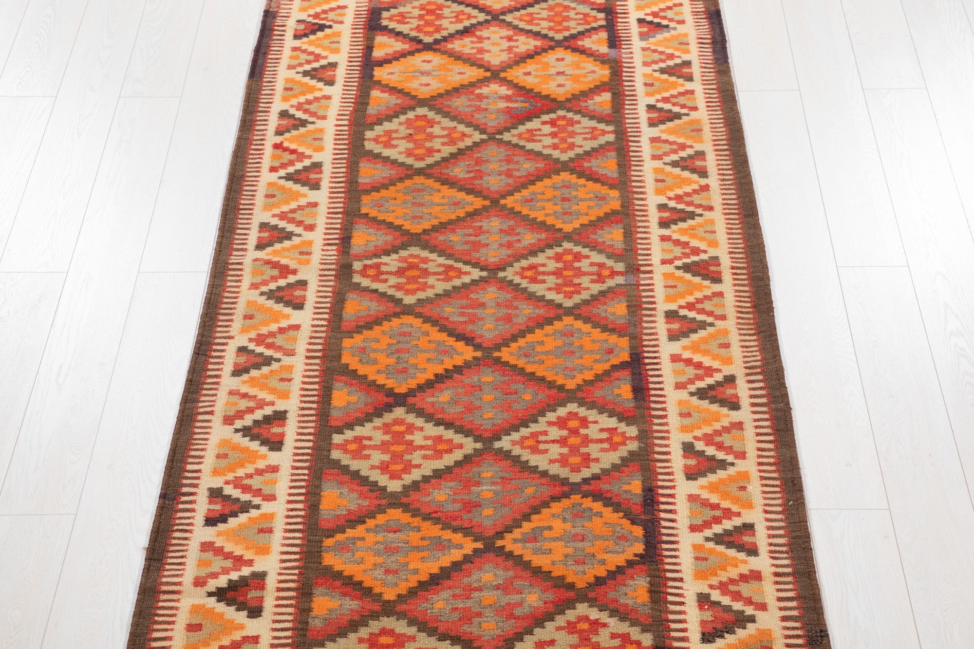 Top-down view of the kilim runner's stacked diamond pattern in red and orange.