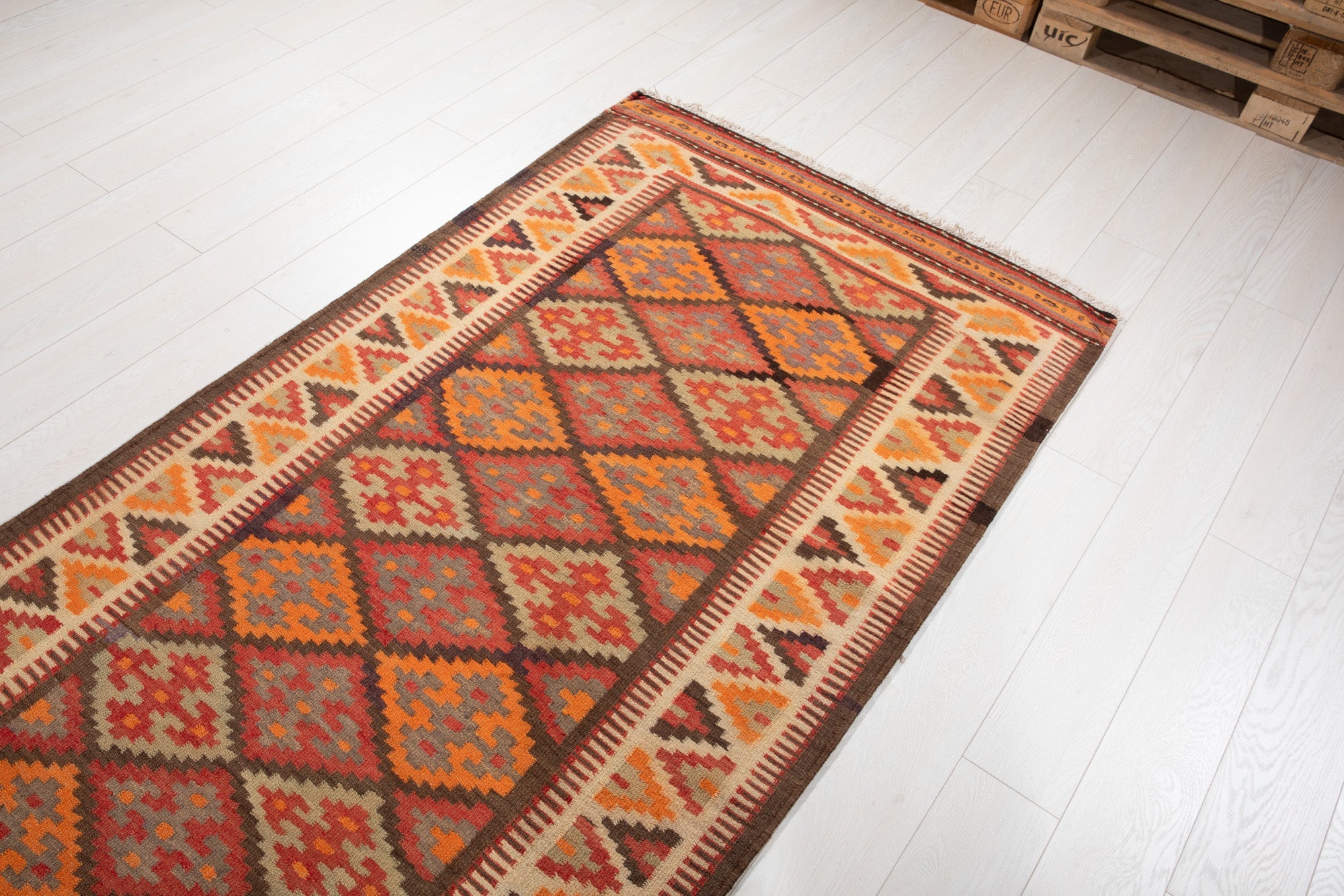 Warehouse angle shot of the kilim rug's diamond pattern with pallets in the background.