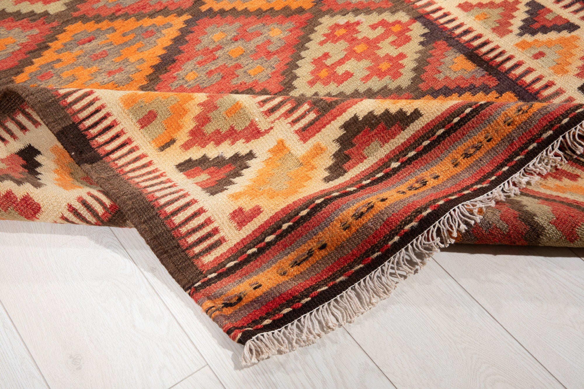 Corner of the kilim runner folded up, showing its fringe and diamond pattern.
