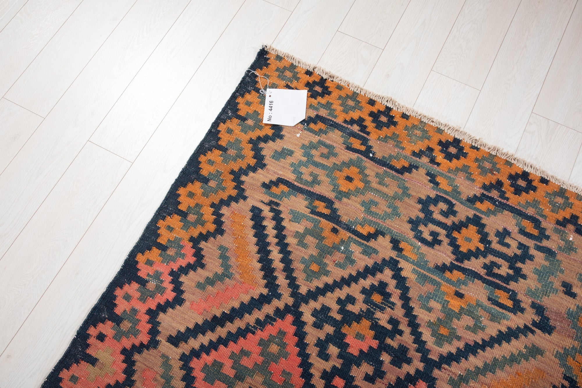 Corner of the antique Persian runner rug with an attached inventory identification tag.