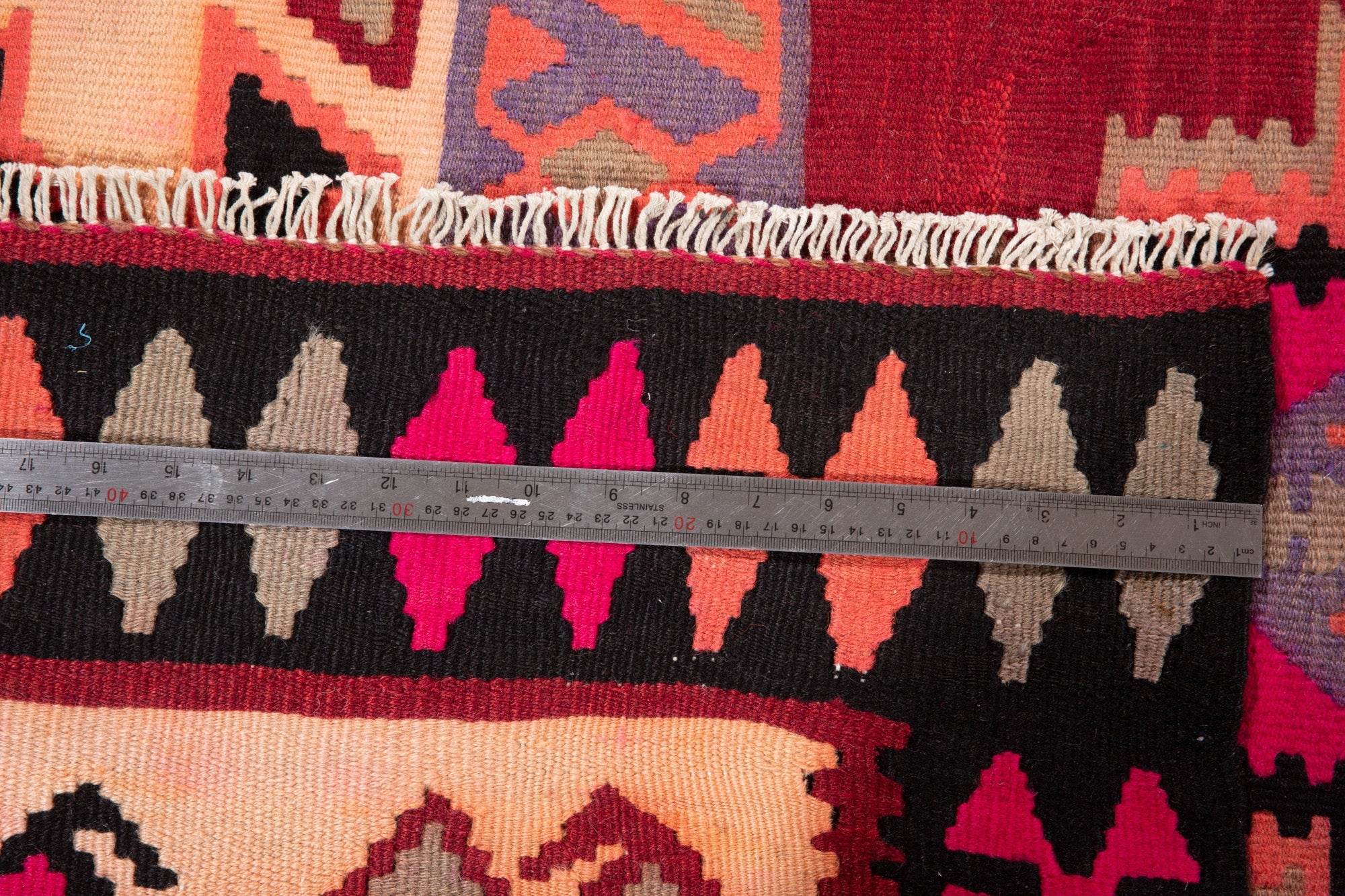 Ruler measuring the kilim's triangle border next to its fringe.