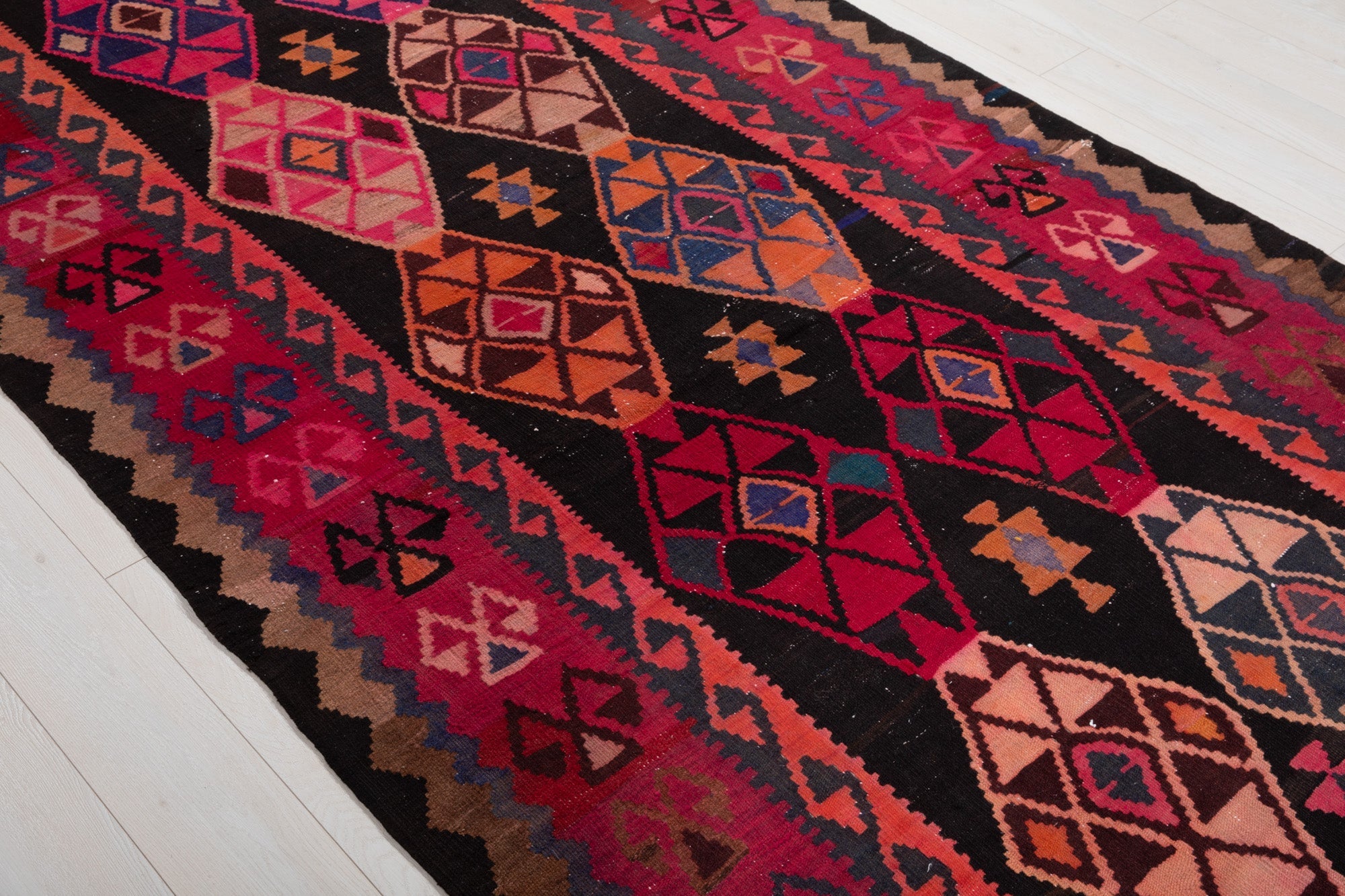 Diagonal close view of the kilim's diamond medallions on a black field.