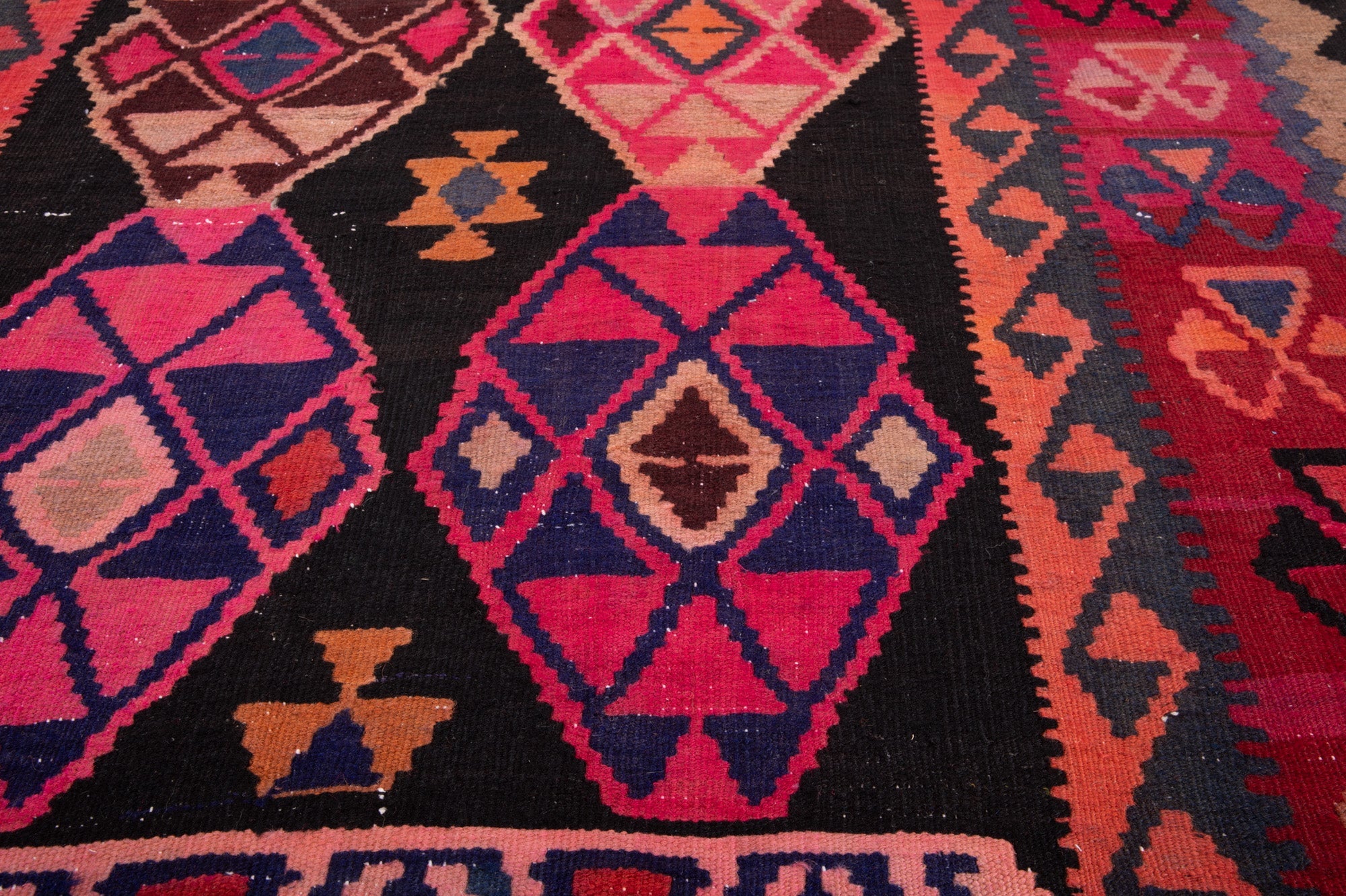 Close-up of the handwoven wool kilim's pink and navy diamond medallions.