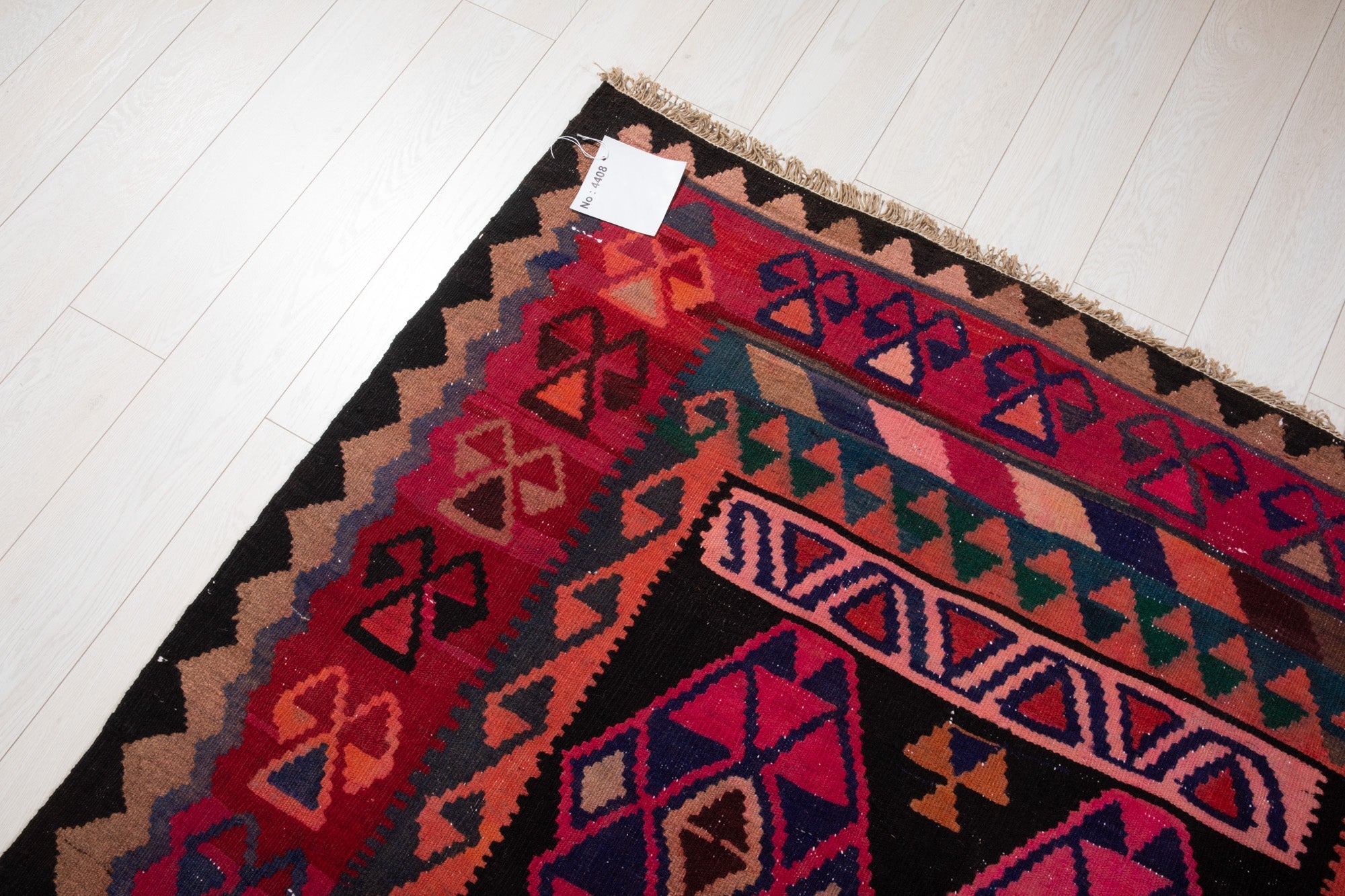 Corner of the vintage Persian Shiraz kilim rug with an attached inventory identification tag.
