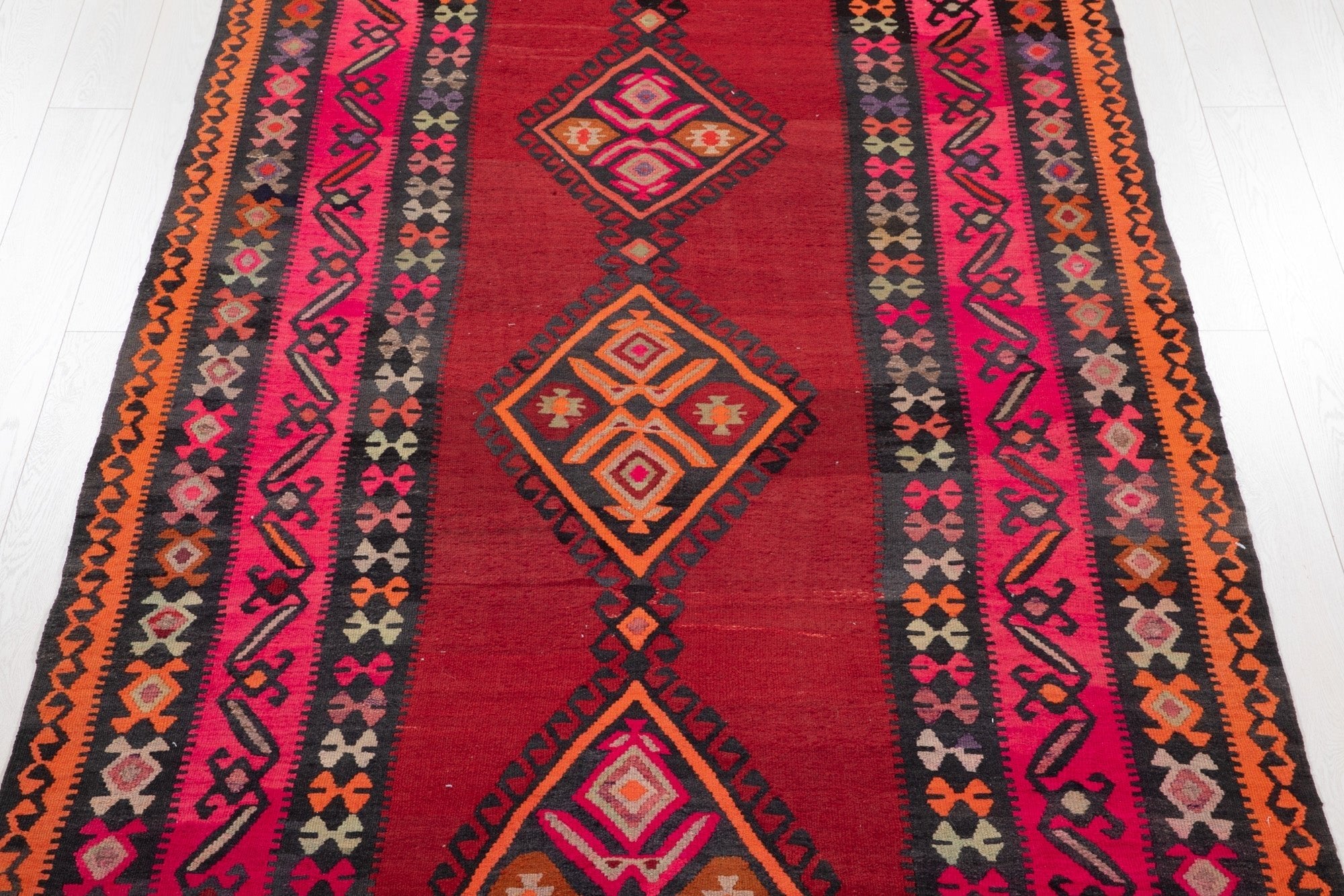 Top-down view of the kilim's stacked diamond medallions on a red field.