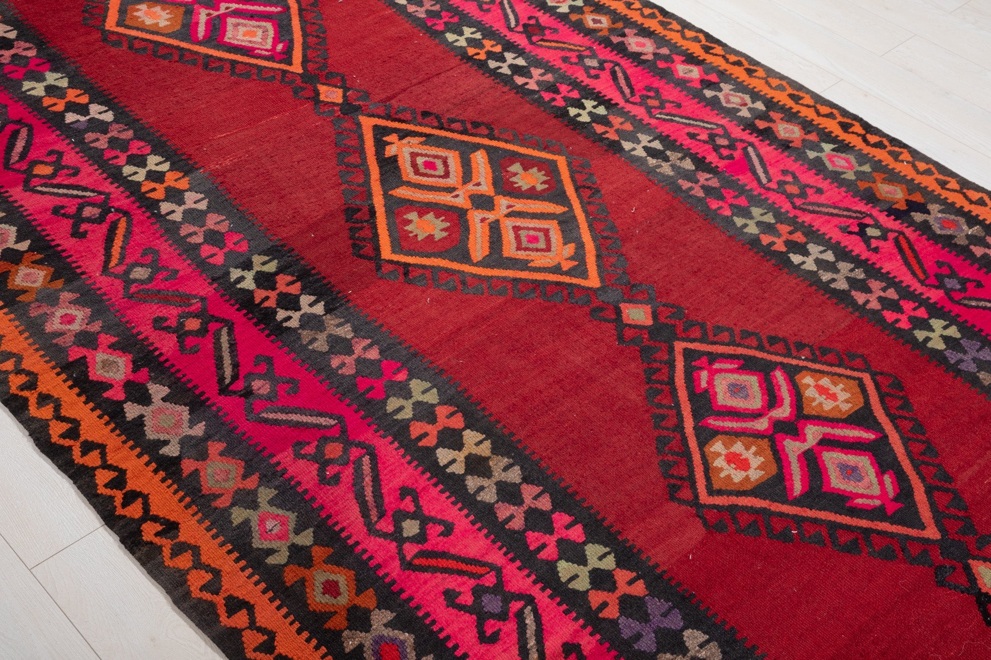 Diagonal close view of the kilim's diamond medallions on a red field.