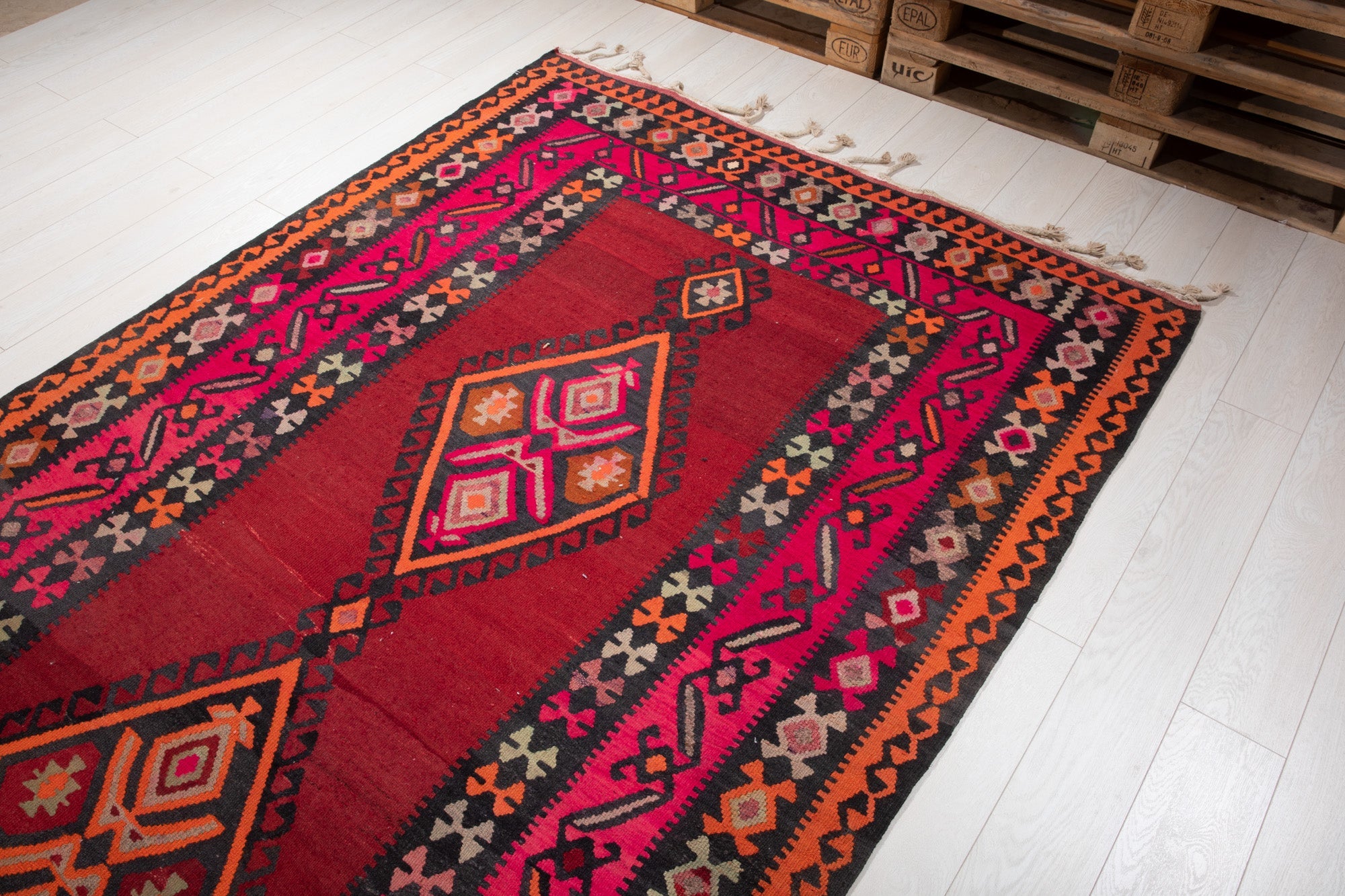 Warehouse angle shot of the kilim rug's diamond medallions with pallets in the background.
