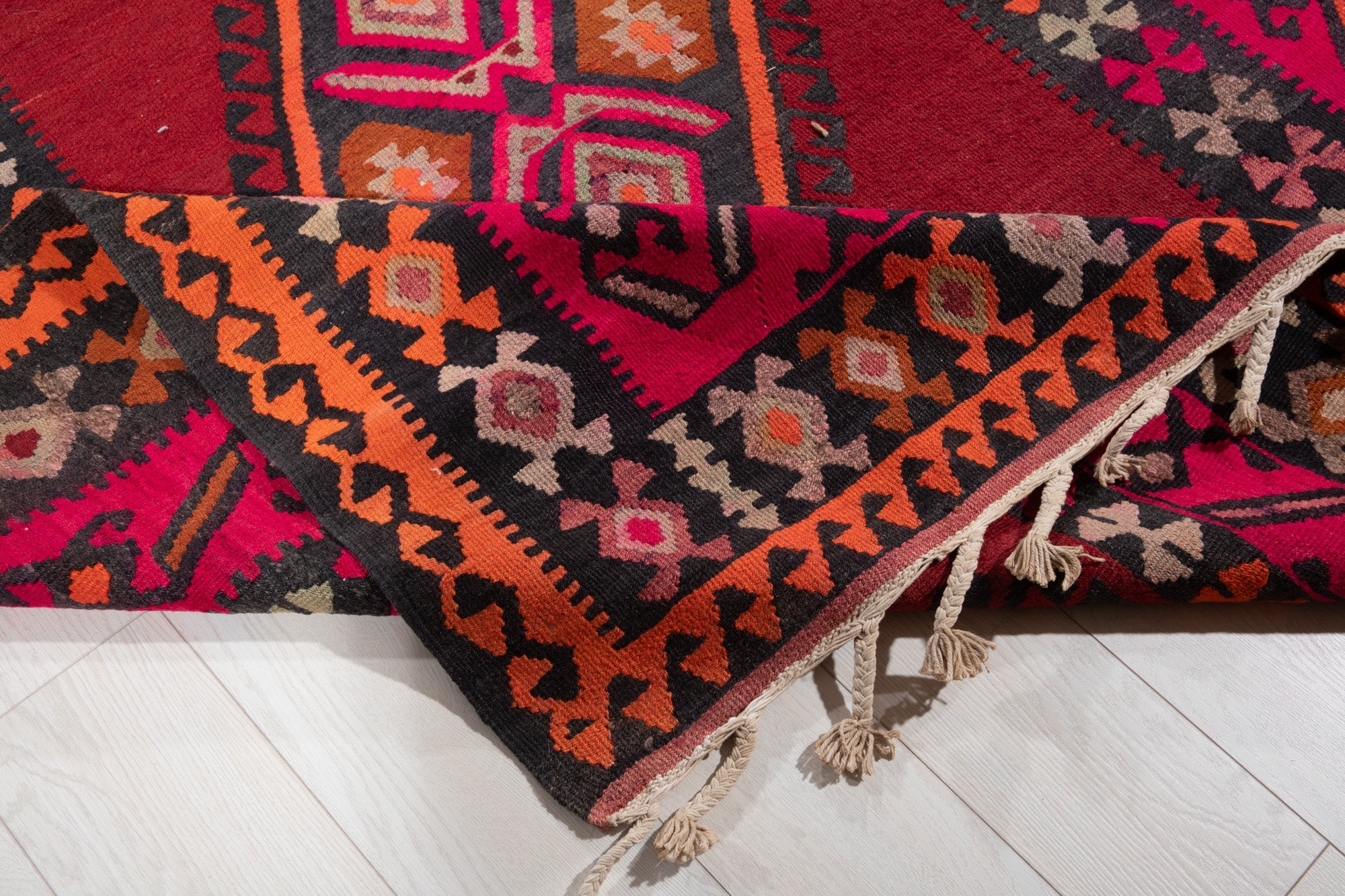 Corner of the kilim rug folded up, showing its border pattern and fringed edge.