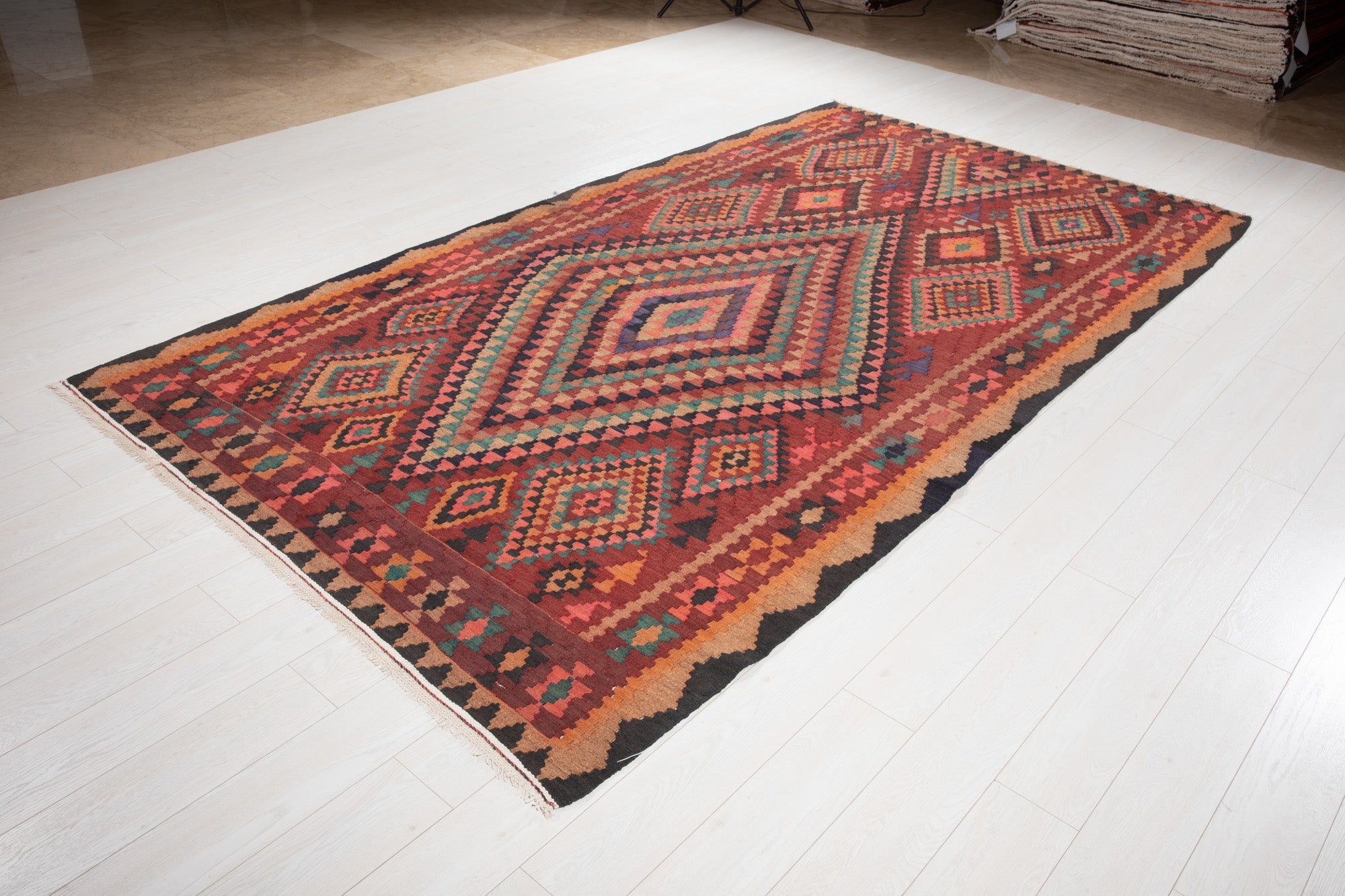 Angled view of the Shiraz Persian kilim's colorful diamond medallion on the showroom floor.