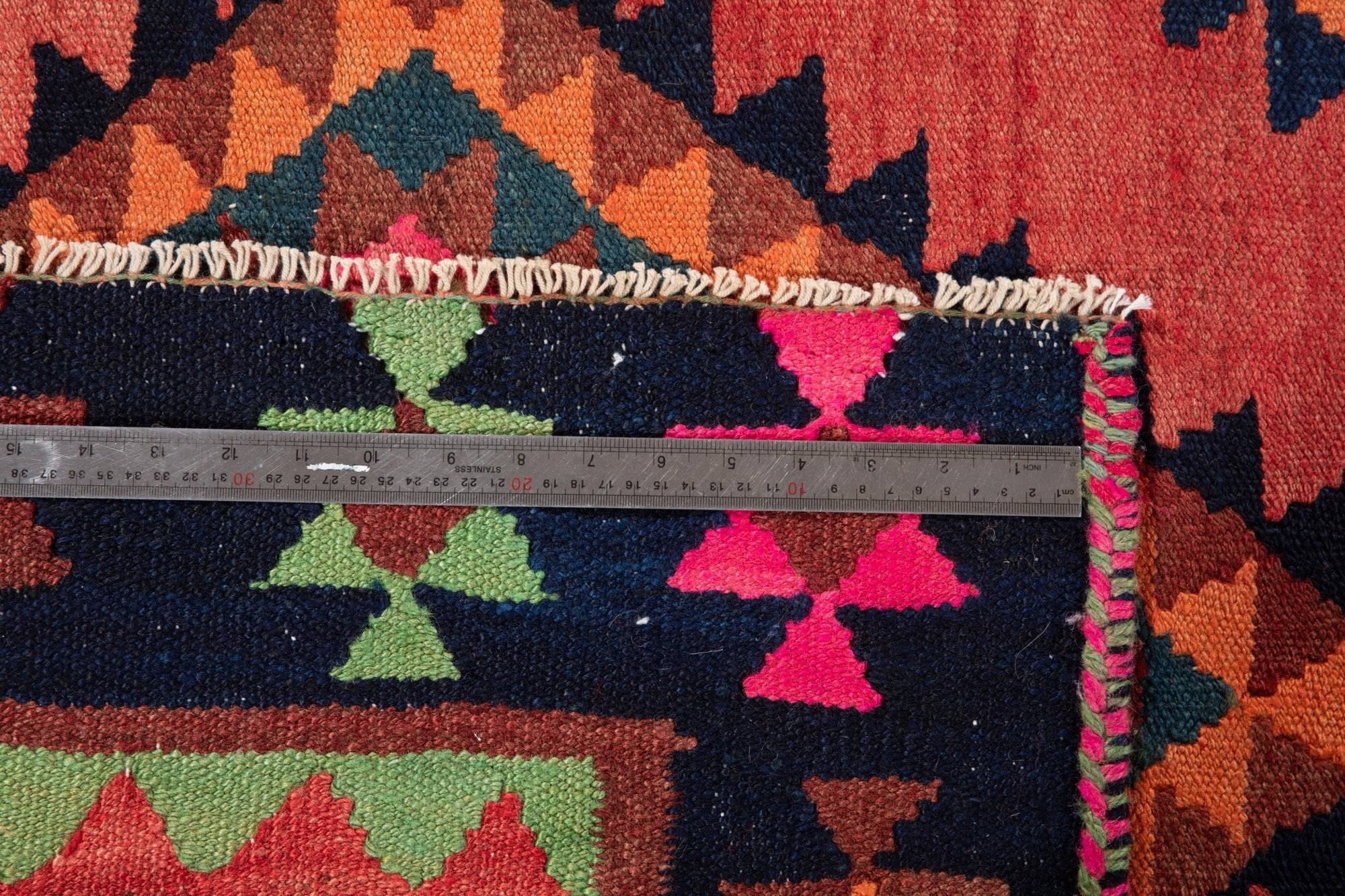 Ruler measuring the kilim's navy border width next to its fringe.