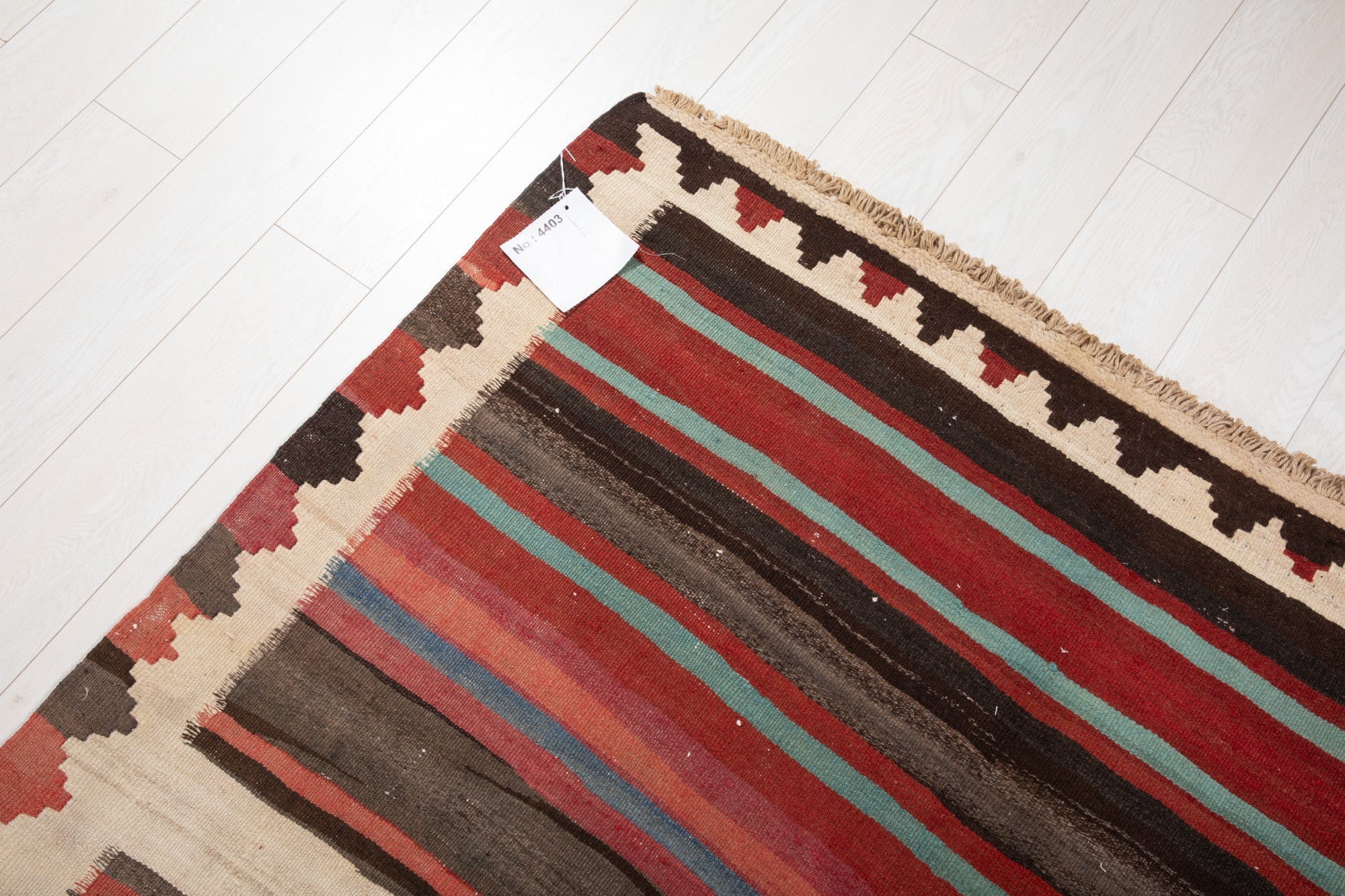 Corner of the vintage Shiraz Persian kilim rug with an attached inventory identification tag.