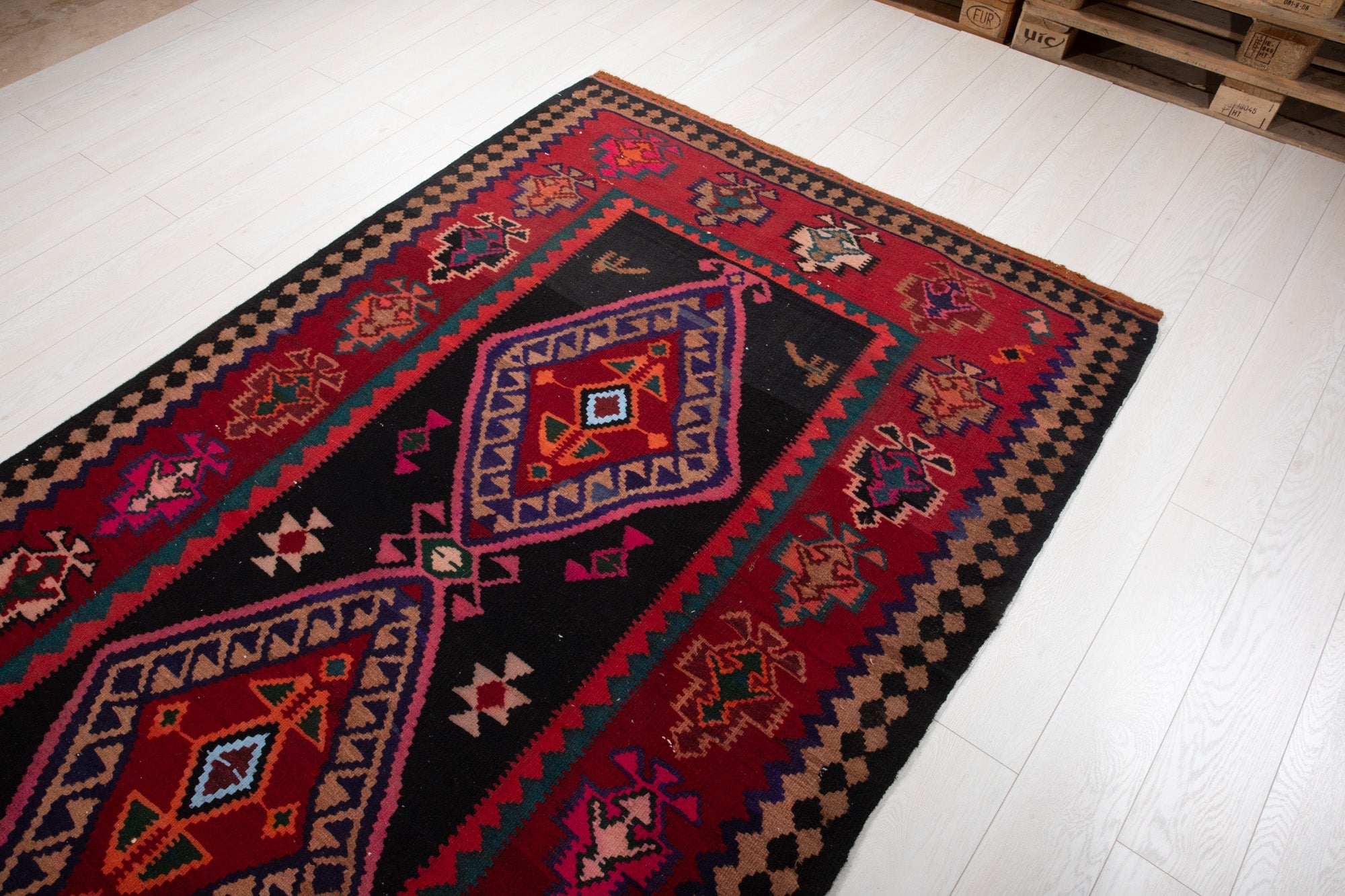 Warehouse angle shot of the kilim rug's diamond medallions with pallets in the background.