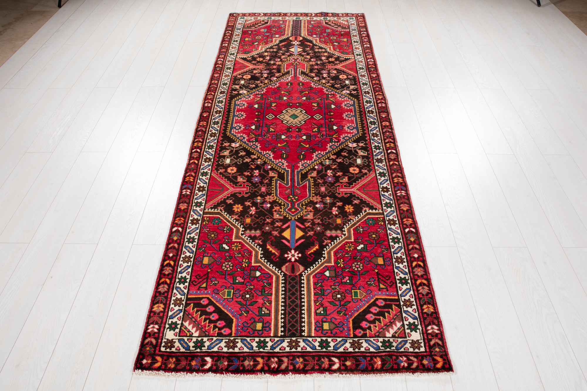 Full top-down view of Hand-Knotted Vintage Wool Runner Rug – 9' 3" x 3' 5" laid flat on a white floor, showcasing its symmetrical tribal design.