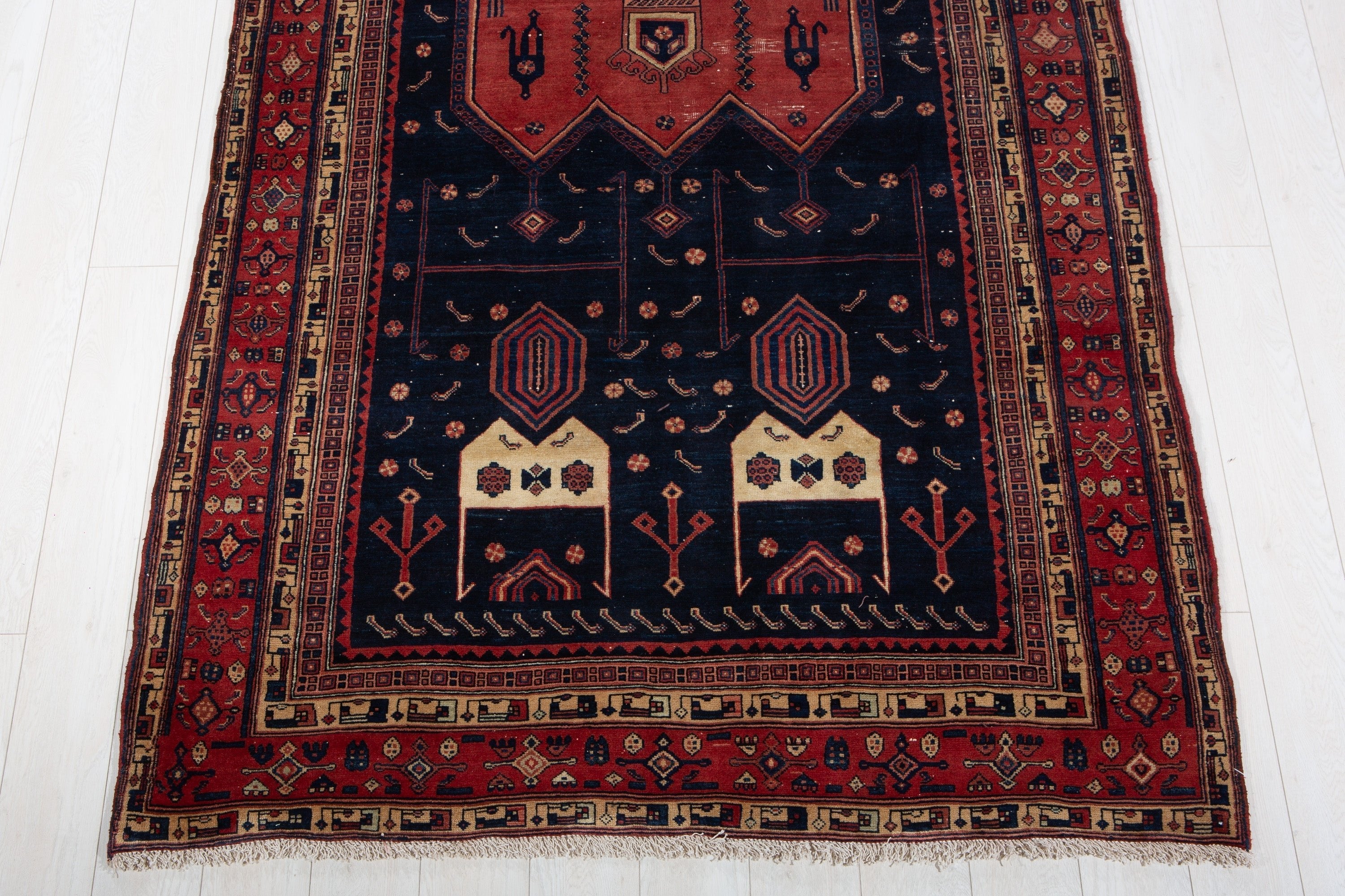One end of the red and navy rug showing the fringe, border, and medallion detail up close.