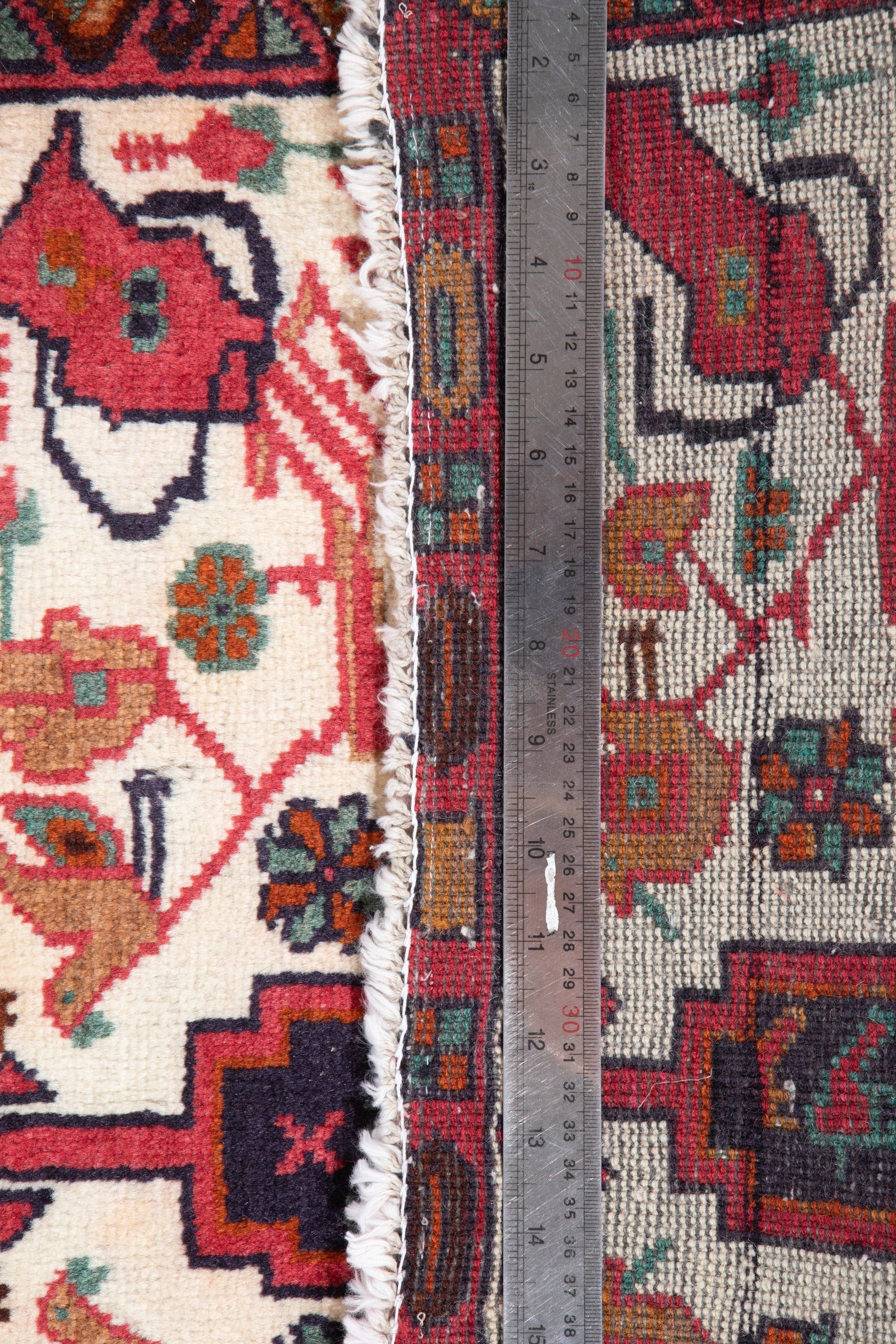 Measuring tape across the rug's width, showing the fringe edge and bird-motif border pattern.
