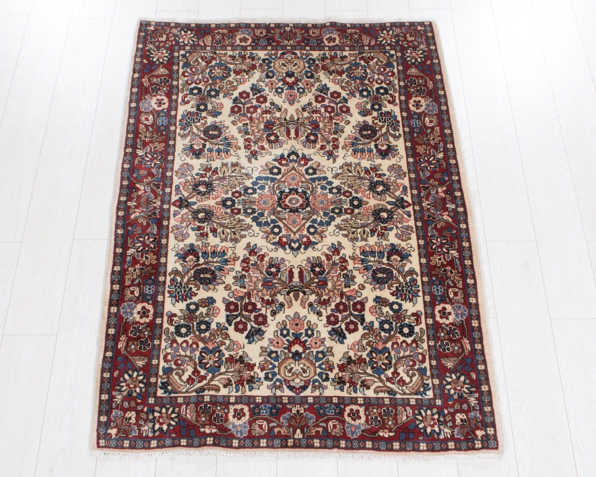Full view of the beige Persian Sarough rug with a red floral border and floral medallion.