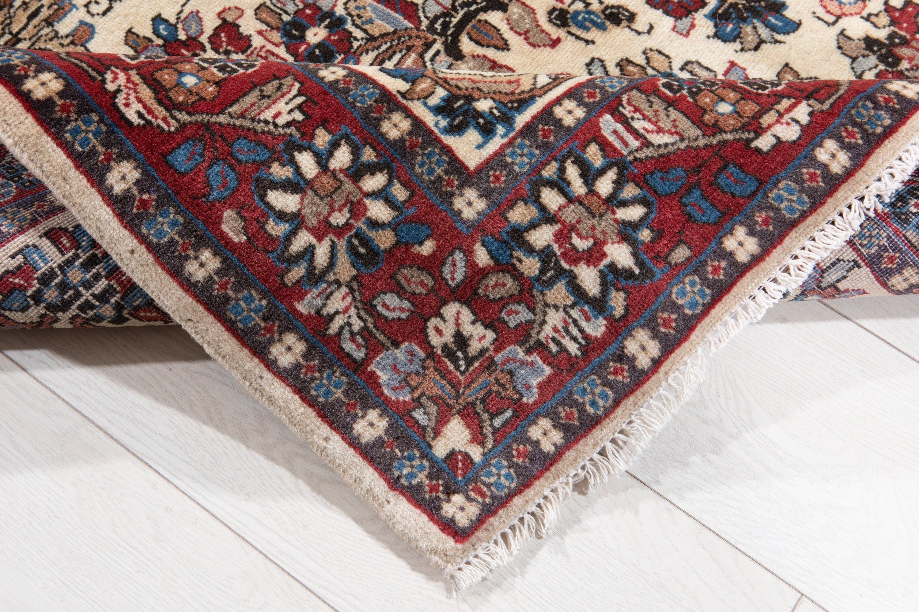 Corner of the rug folded up, showing the red border, fringe, and floral corner design.