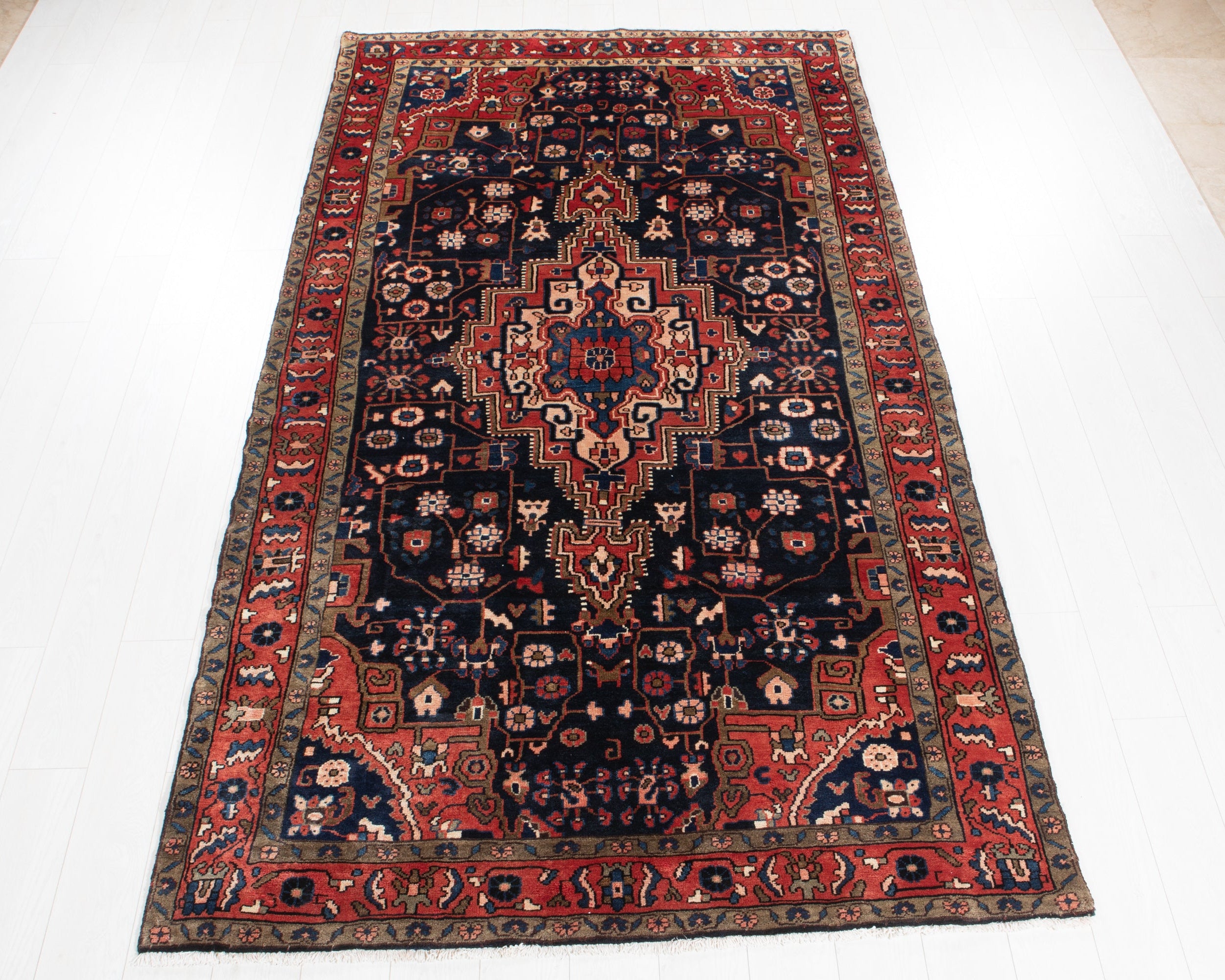A rectangular traditional Persian Malayer Hamadan area rug with a dark navy blue field, red borders, and a central medallion, laid flat on a white floor.
