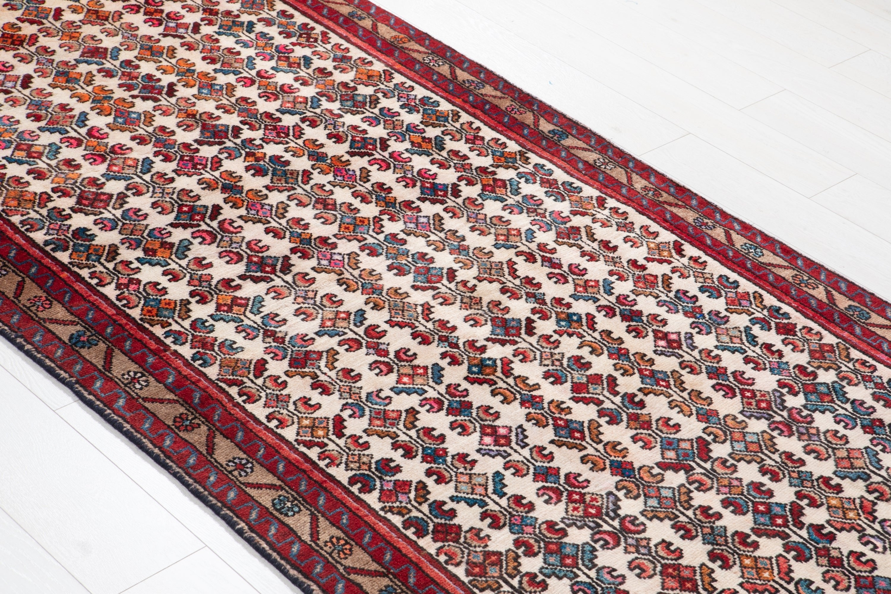 Angled view of Hamadan Persian runner showing repeating diamond motifs in red and cream