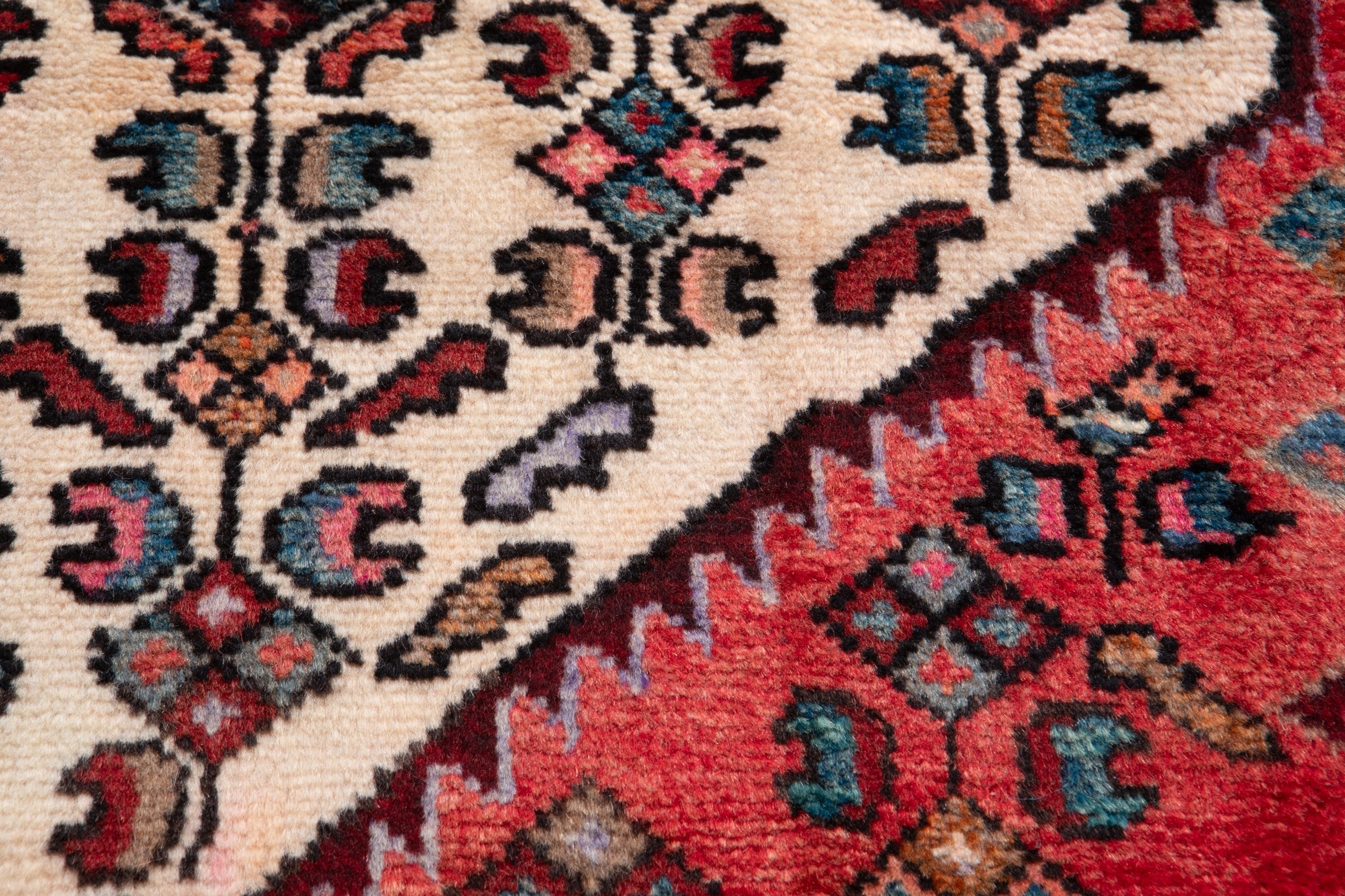 Macro detail of hand-knotted motifs on Hamadan Persian runner, cream, red, and teal tones