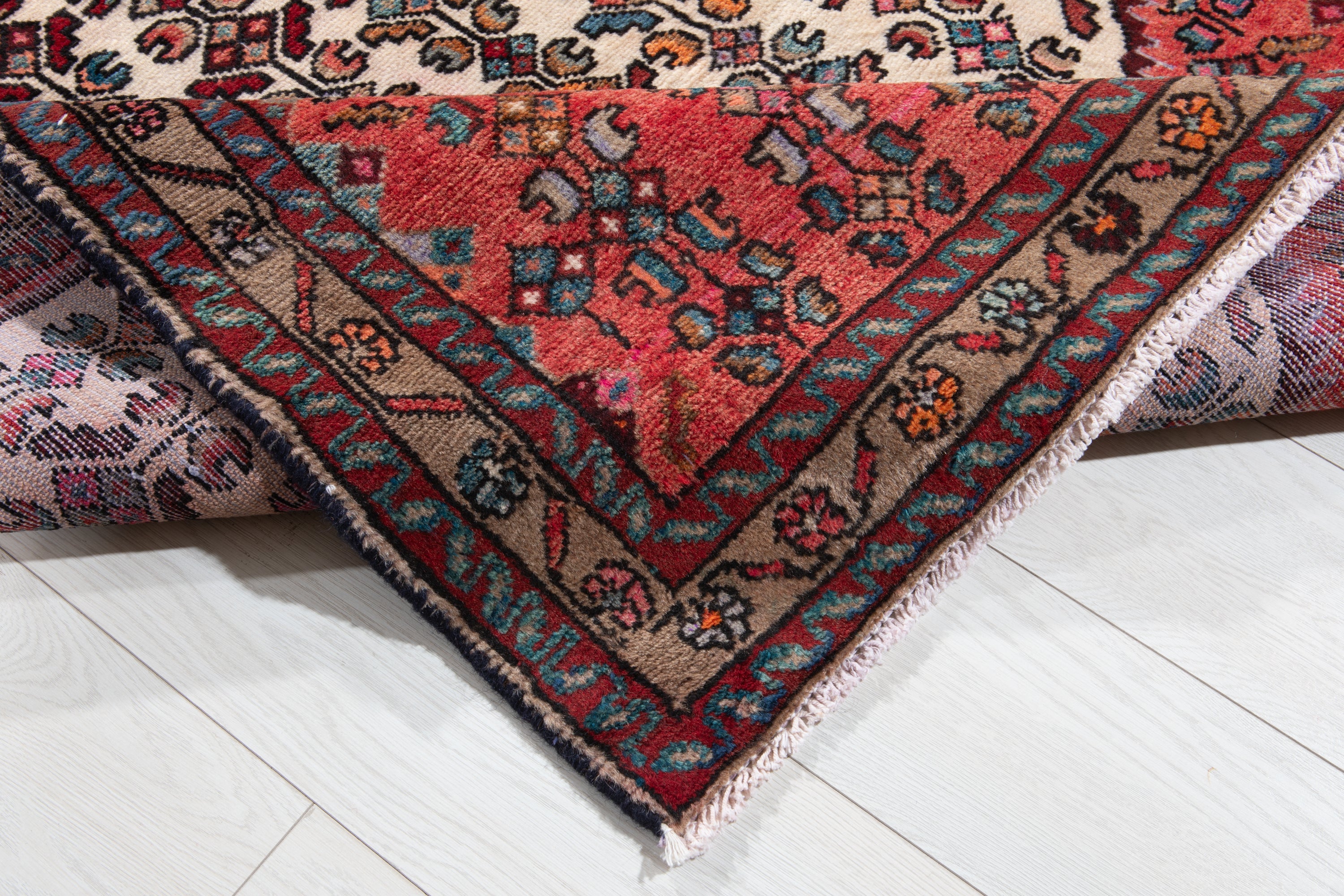Folded corner of Hamadan Persian runner showing pile, woven back, and fringe