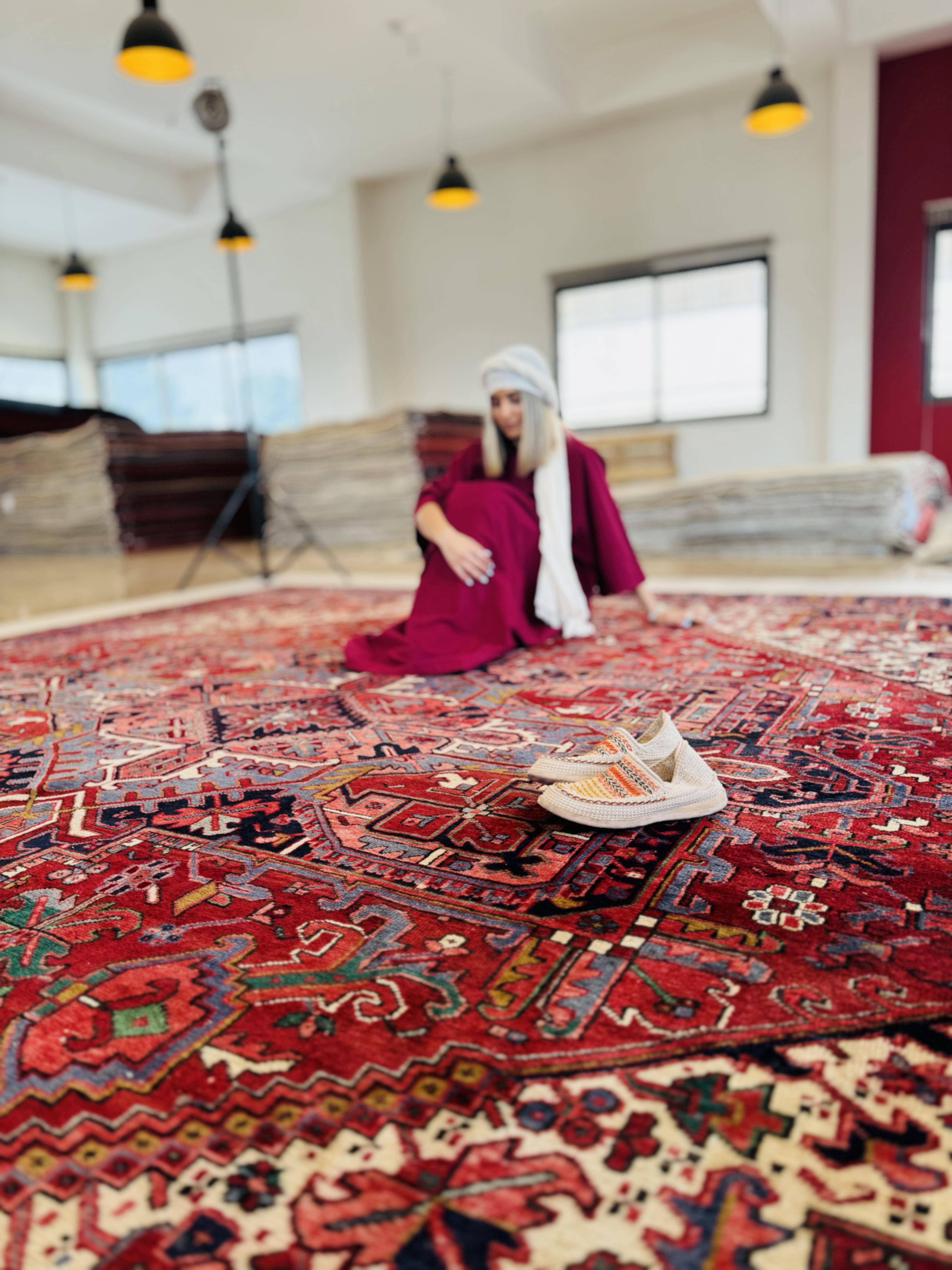 Wide lifestyle shot of a person kneeling on the rug with sneakers placed on it.