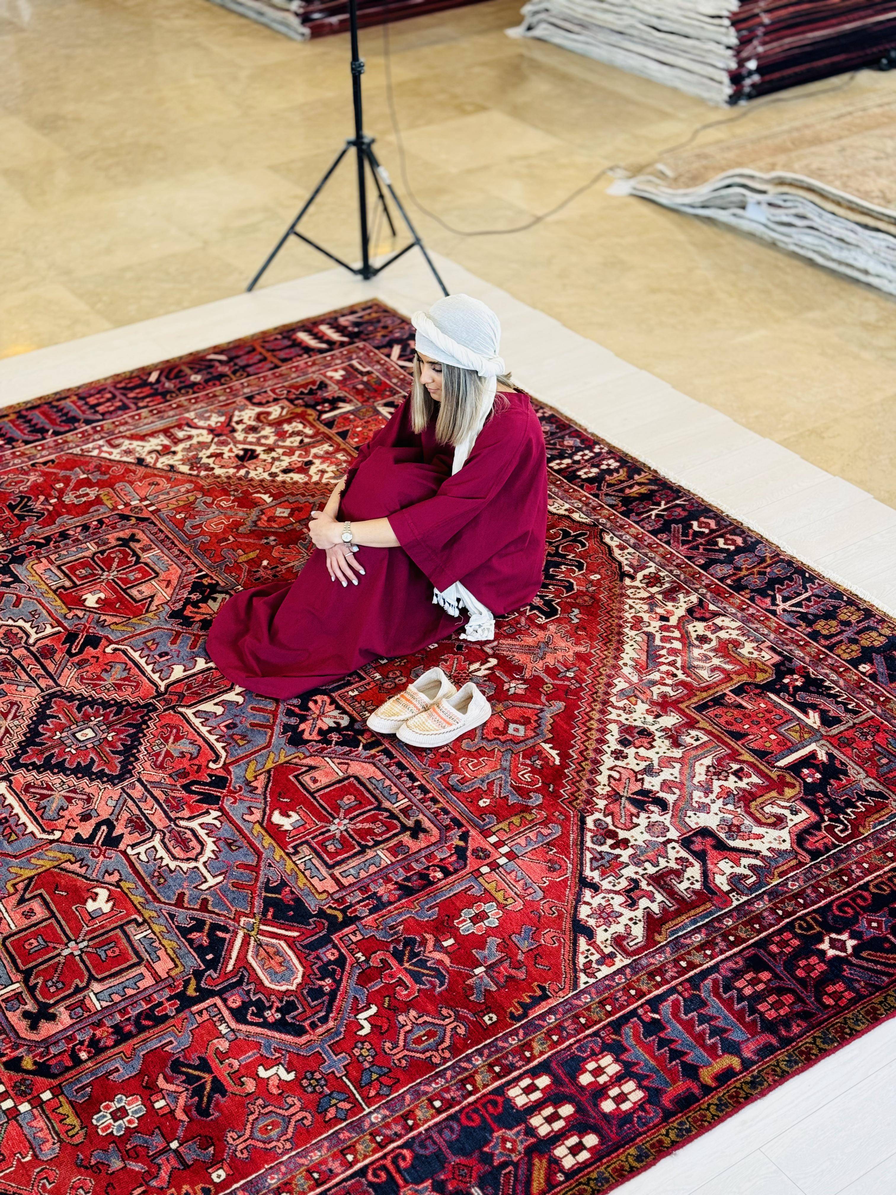 Lifestyle shot of a person sitting on the rug in a showroom with rolled rugs behind them.