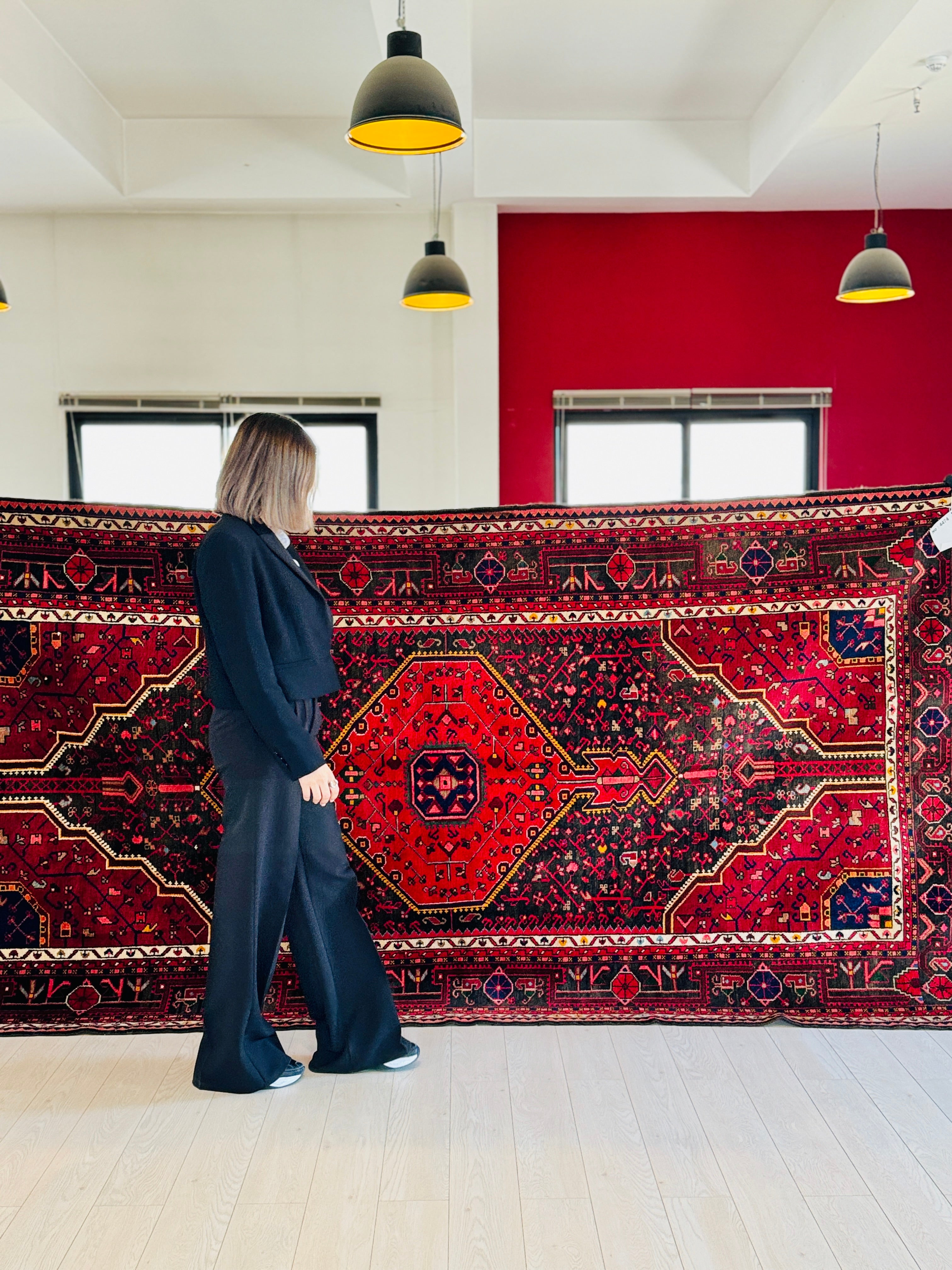 Woman holding Hand-Knotted Vintage Wool Area Rug – 10' 6" x 5' 5" showcasing its bold red medallion and traditional motifs in a modern interior.