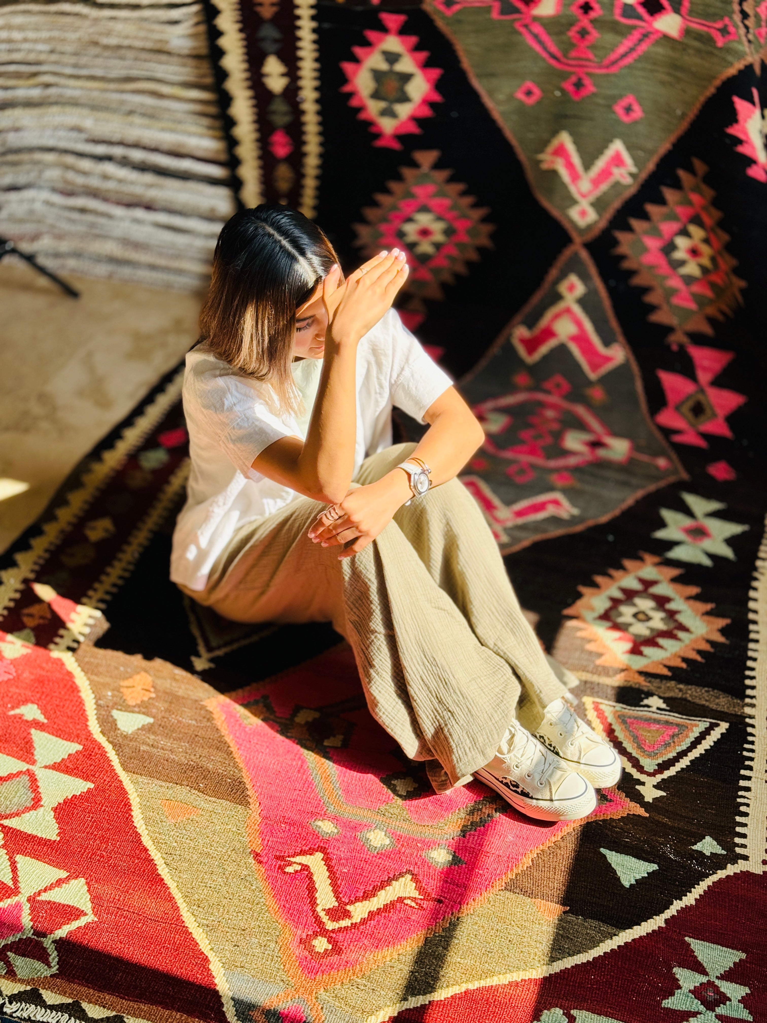 Lifestyle shot of a woman sitting on the vintage Persian kilim rug, showing its tribal diamond pattern up close.