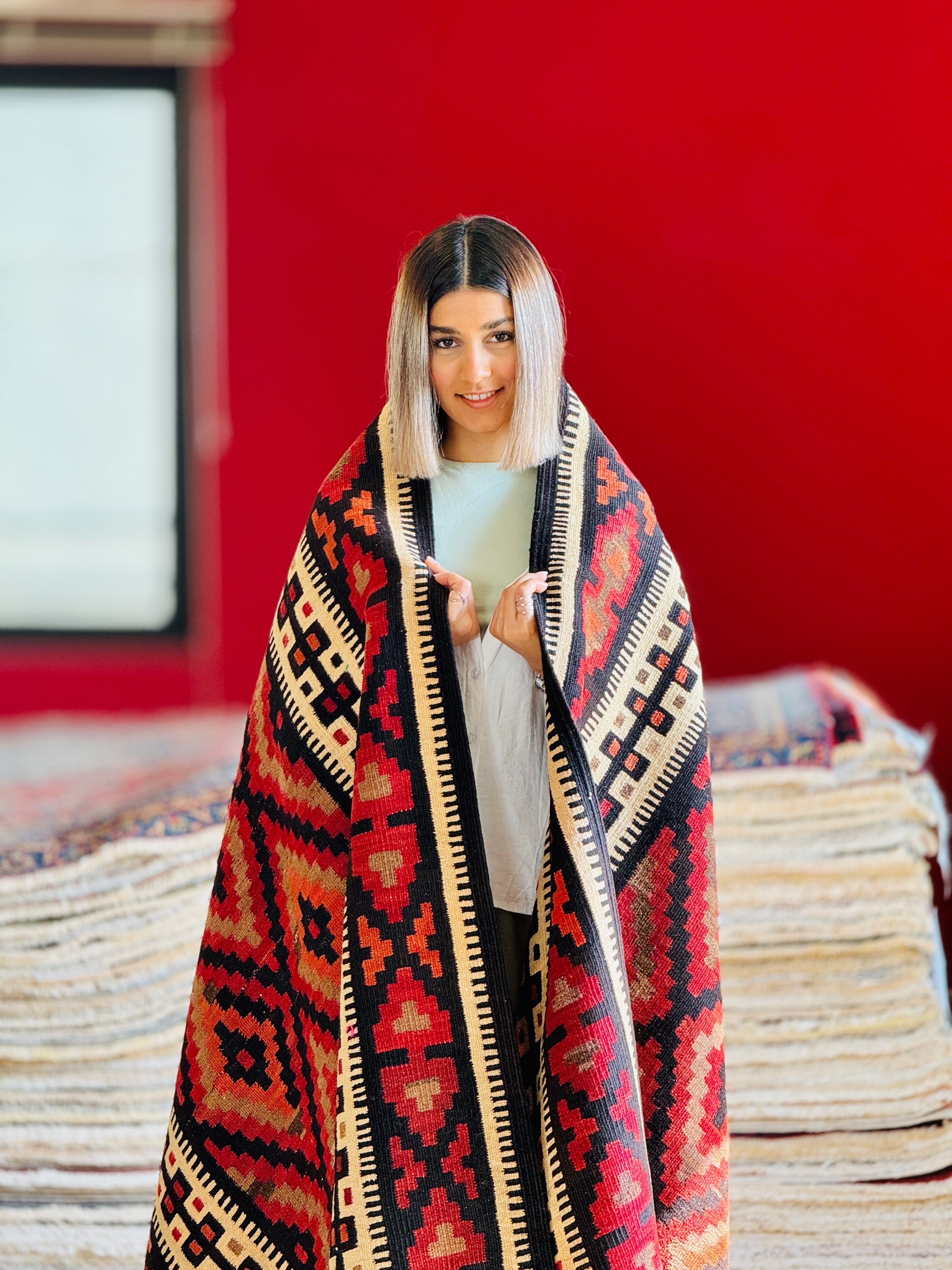 Lifestyle shot of a woman wrapped in the red kilim rug like a blanket.
