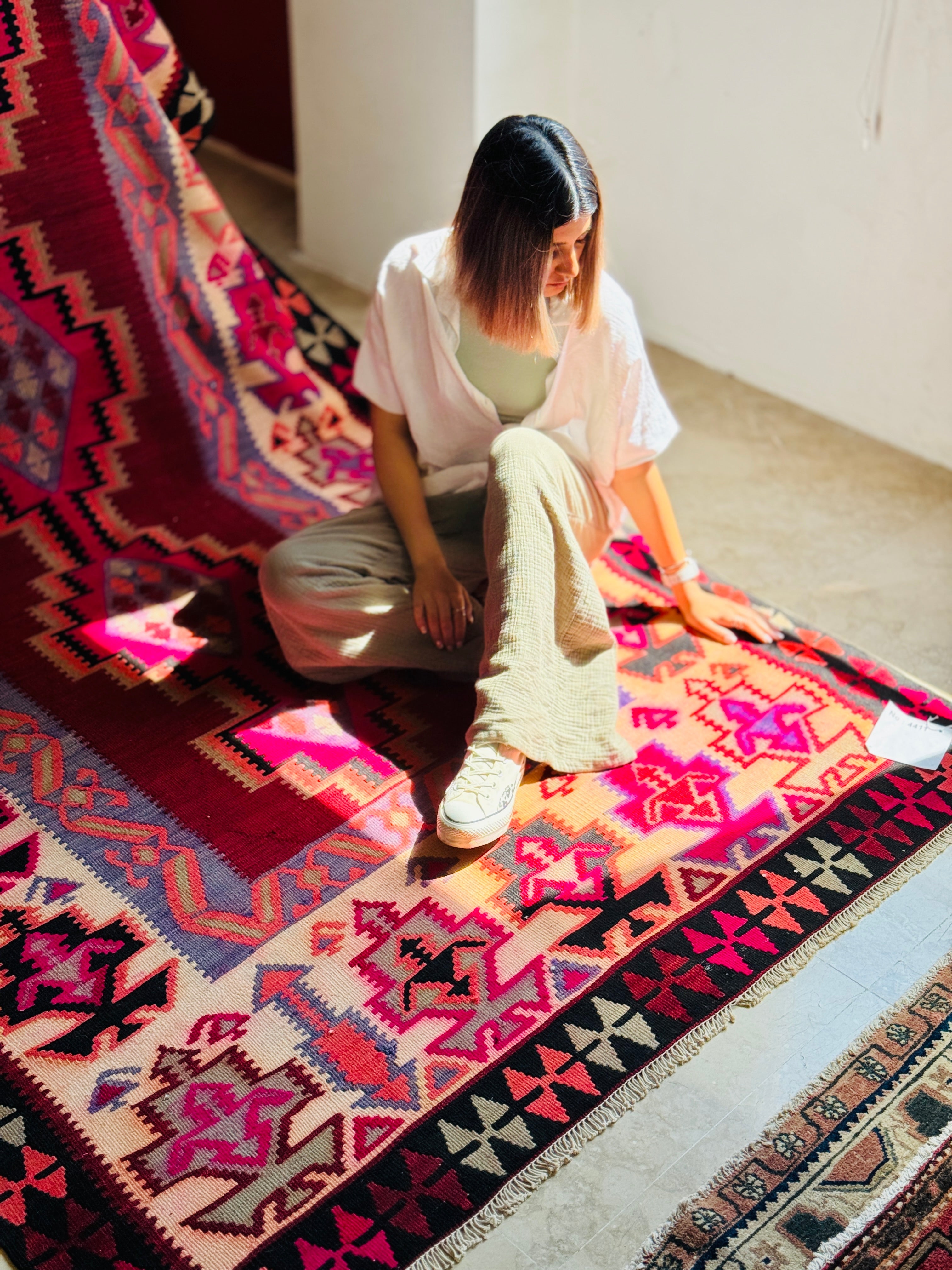 Overhead lifestyle shot of a woman sitting on the pink kilim rug in sunlight.
